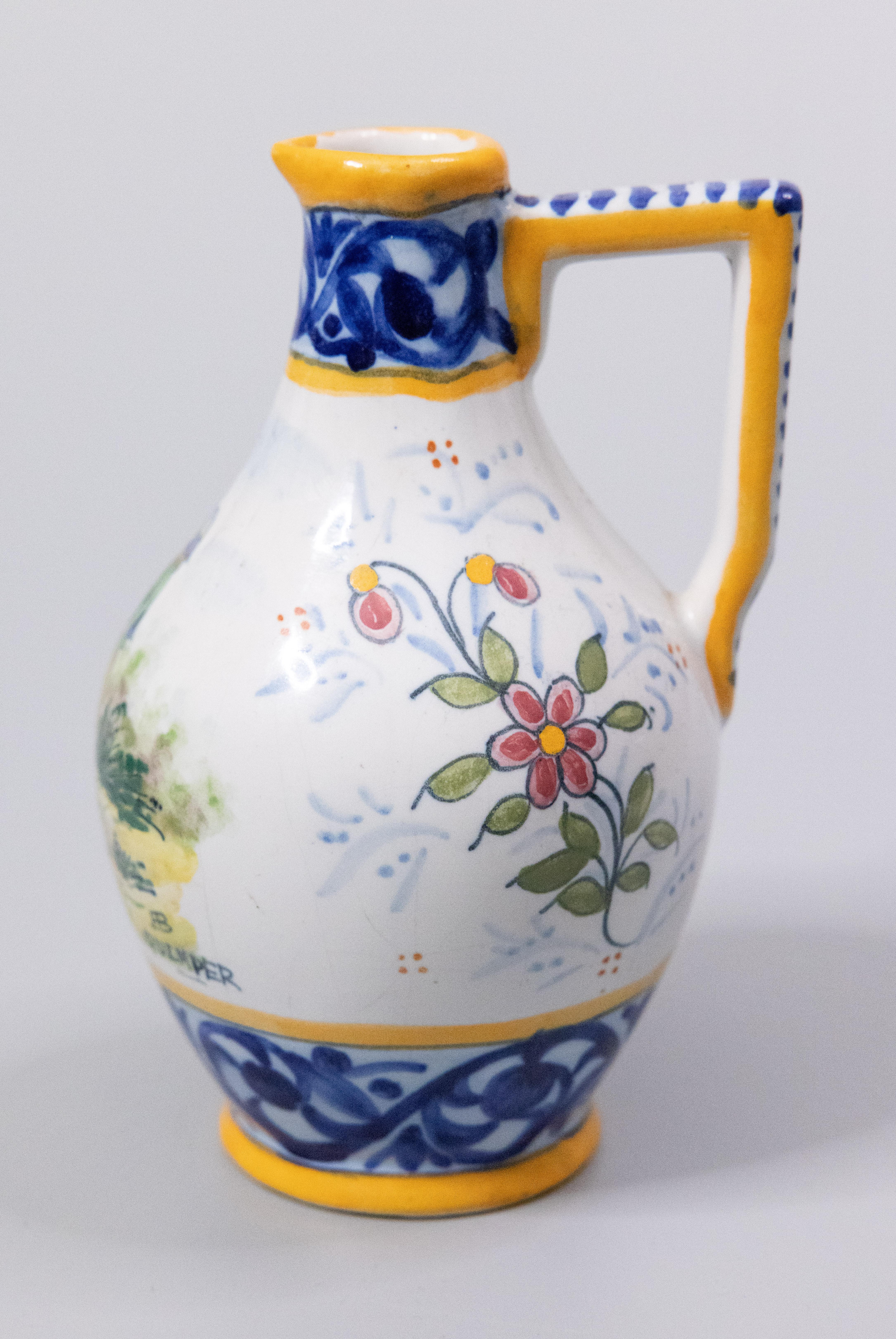A charming petite antique French faience Quimper pitcher or small ewer, circa 1910. Maker's mark on reverse. This lovely pitcher is decorated with a hand painted traditional Breton man surrounded by a floral pattern in beautiful vibrant colors. It's