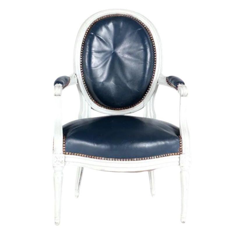 Paire de petites chaises anciennes de style Louis XVI, sculptées et peintes, avec sièges, dossiers et accoudoirs en cuir marine. Les dossiers, les sièges et les accoudoirs des chaises sont ornés d'une garniture en forme de tête de clou. Les pieds et