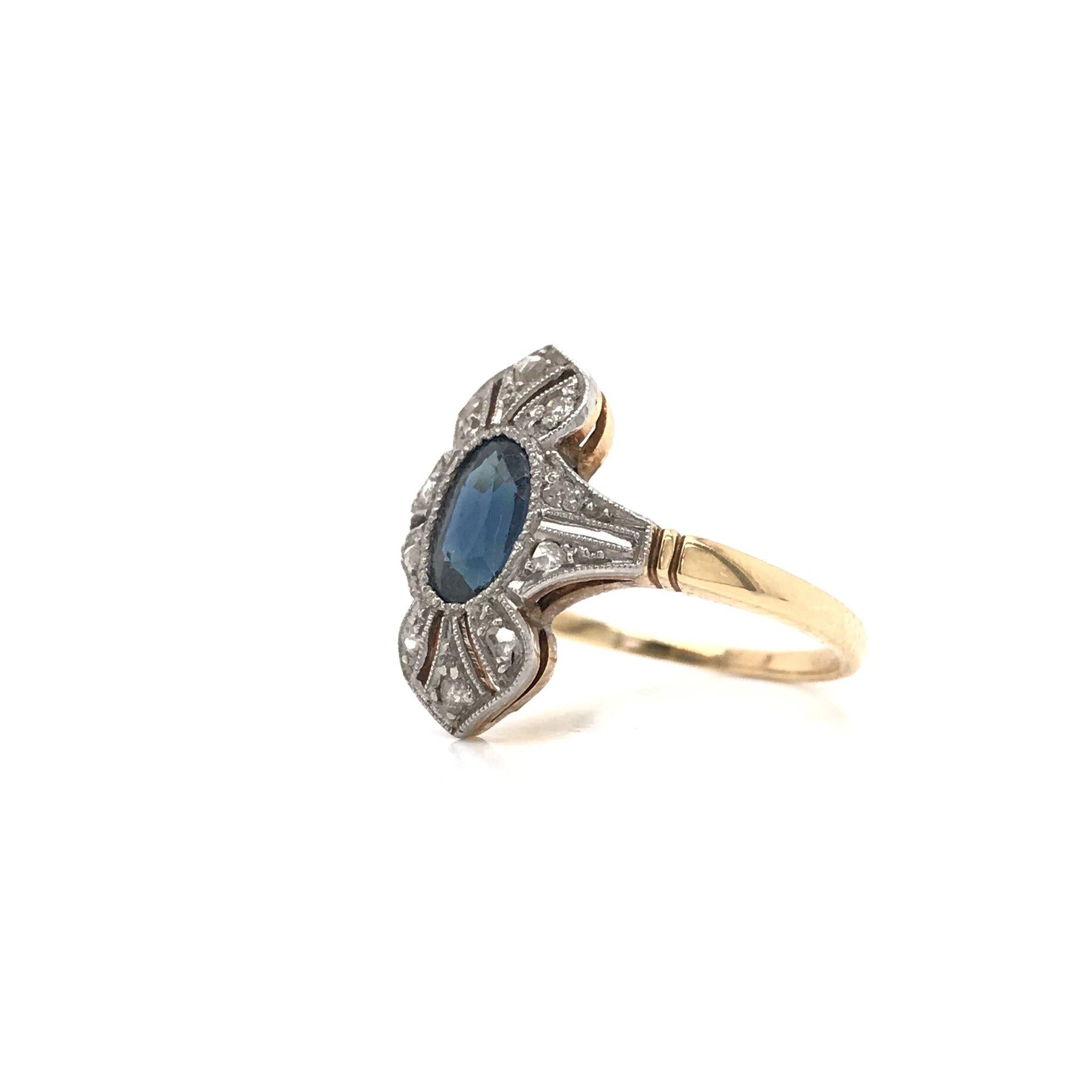 This antique piece was handcrafted sometime during the Art Deco design period ( 1920-1940 ). The shank and gallery of the ring are 14k yellow gold and the head is 14k white gold. The ring features a central oval cut blue sapphire. The setting also