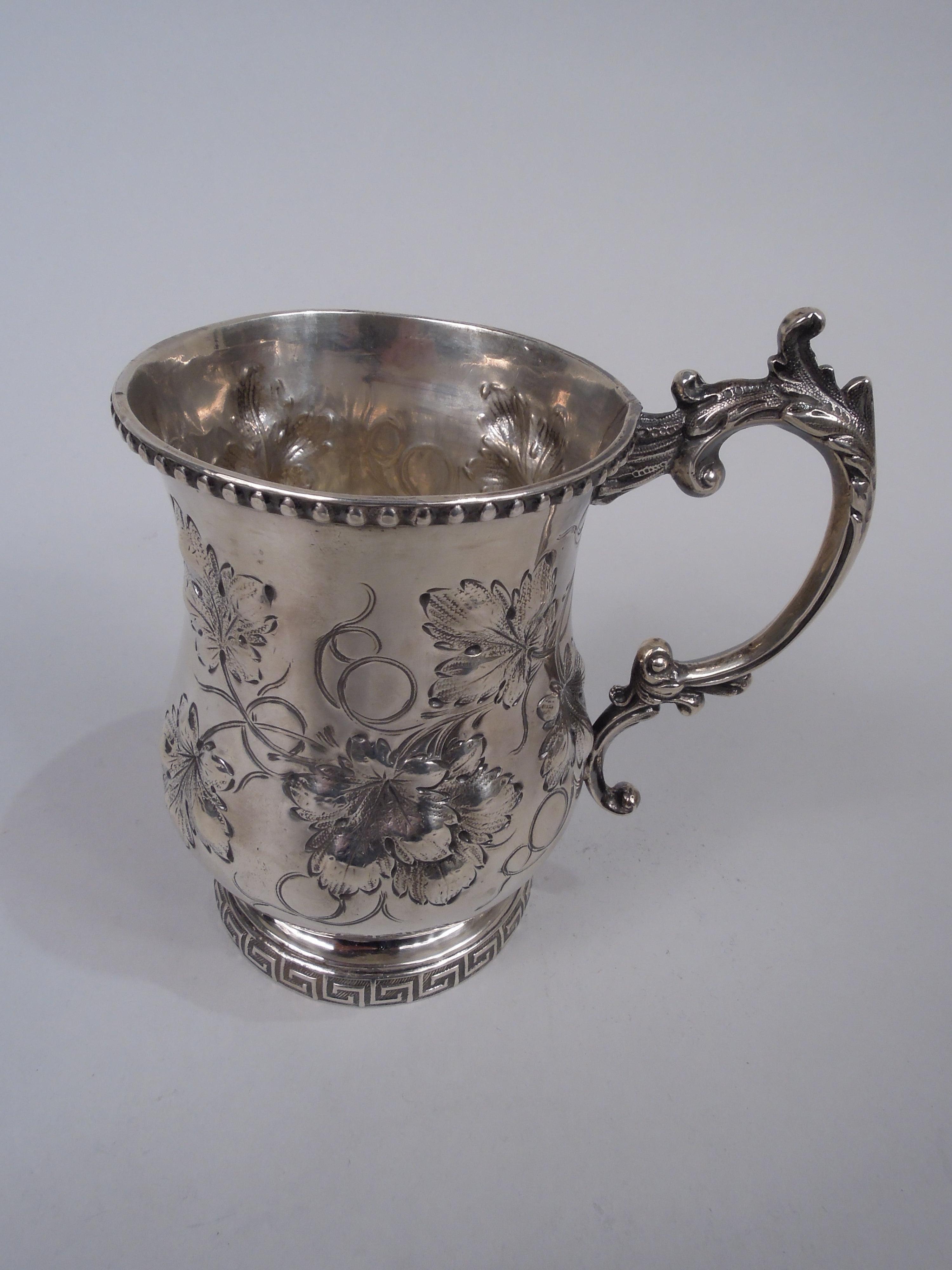 Victorian Classical coin silver baby cup, ca 1860. Baluster bowl with cast leaf-capped double-scroll handle and raised foot. Chased leaf and tendrils forming frame (vacant). Beaded and Greek key rims. Unidentified marks associated with Philadelphia