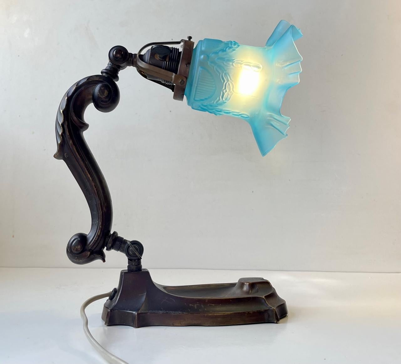 A beautifully crafted and detailed Table, Piano or Mantle Lamp. Distinct Art Nouveau styling. Its pivoting and fully adjustable. Made from patinated 'embossed'/molded bronze and has a wavy frosted light blue glass shade modulated with impressions of