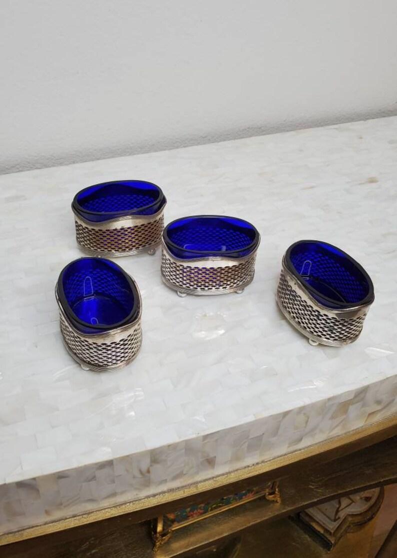 A remarkable four piece collection of rare open salts, featuring oval shaped footed pierced silver exteriors, retaining the original fitted deep cobalt blue glass open top liners.

Well marked, signed with manufacturer's hallmarks to verso: 
Lion