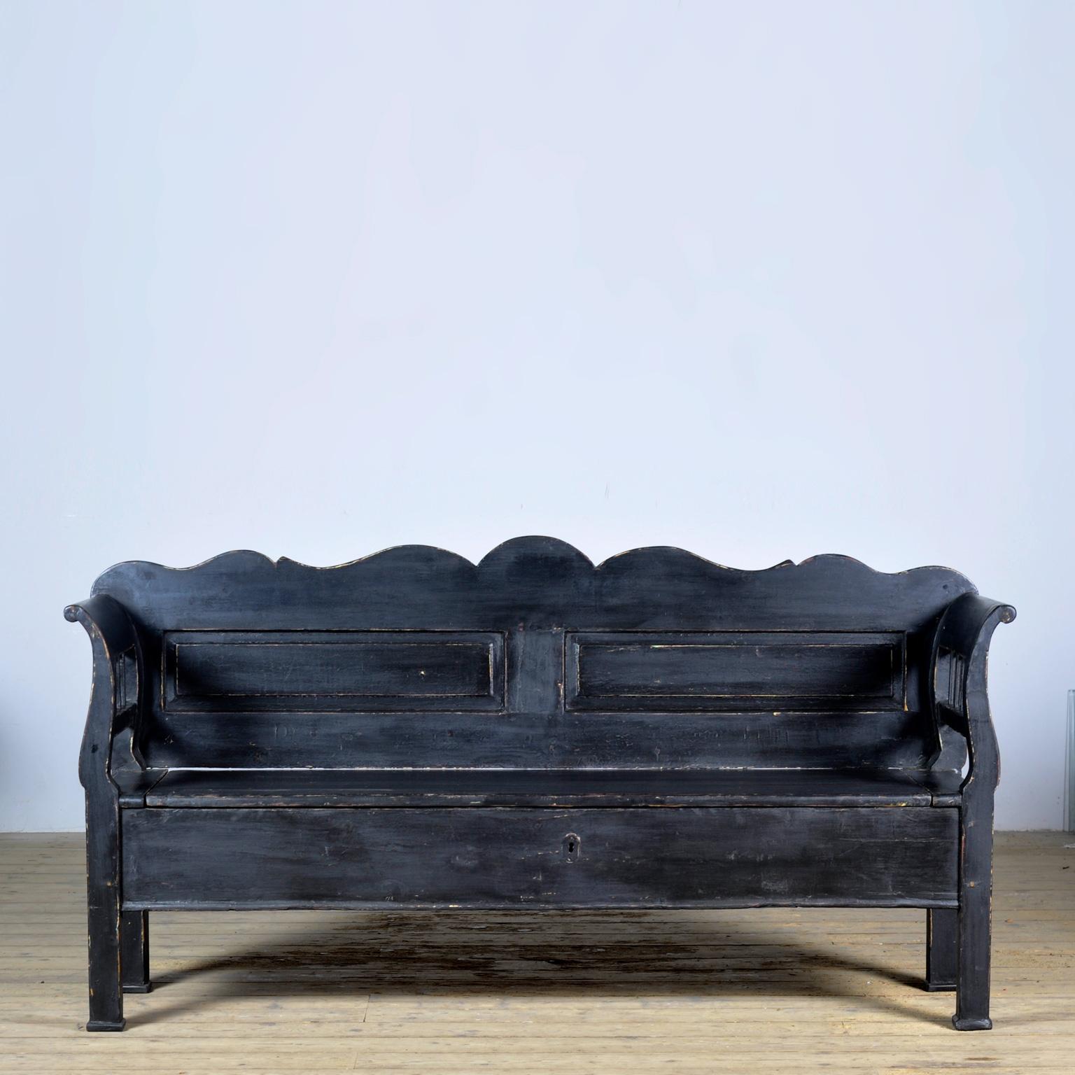 Un'affascinante panchina ungherese del 1900 circa. Con il tempo e l'uso, la vernice nera si è consumata in alcuni punti del legno. Con un vano portaoggetti sotto il sedile diviso in due scomparti. La panchina è stabile e priva di tarli.