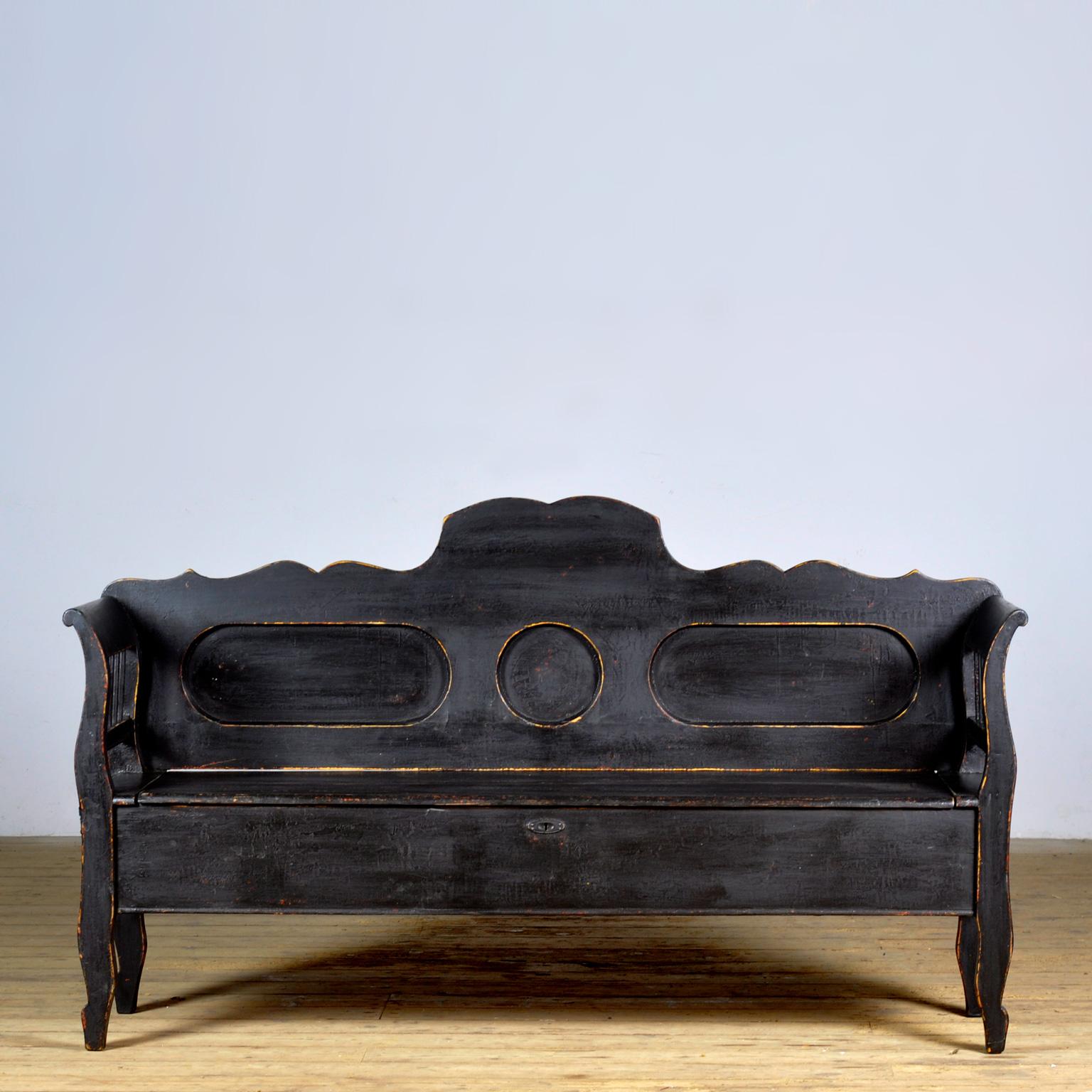 Un charmant banc hongrois datant d'environ 1900. Au fil du temps et de l'utilisation, la peinture noire s'est usée par endroits jusqu'au bois. Avec un espace de rangement sous le siège divisé en deux compartiments. Le banc est stable et exempt de