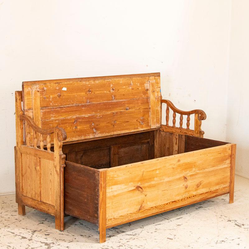 The years of use have deepened the warm patina of the pine, aging gracefully through the years. The turned spindles along the back and arms add to its appeal. Notice the seat is hinged, creating great storage space for items that need to be