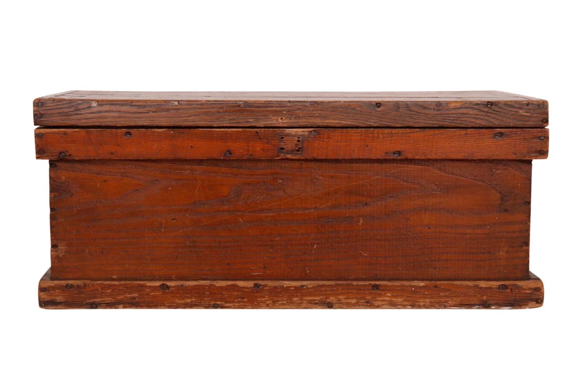 An antique blanket chest made of pine. Constructed with plank wood secured with nails. The lid hinges open to reveal storage.