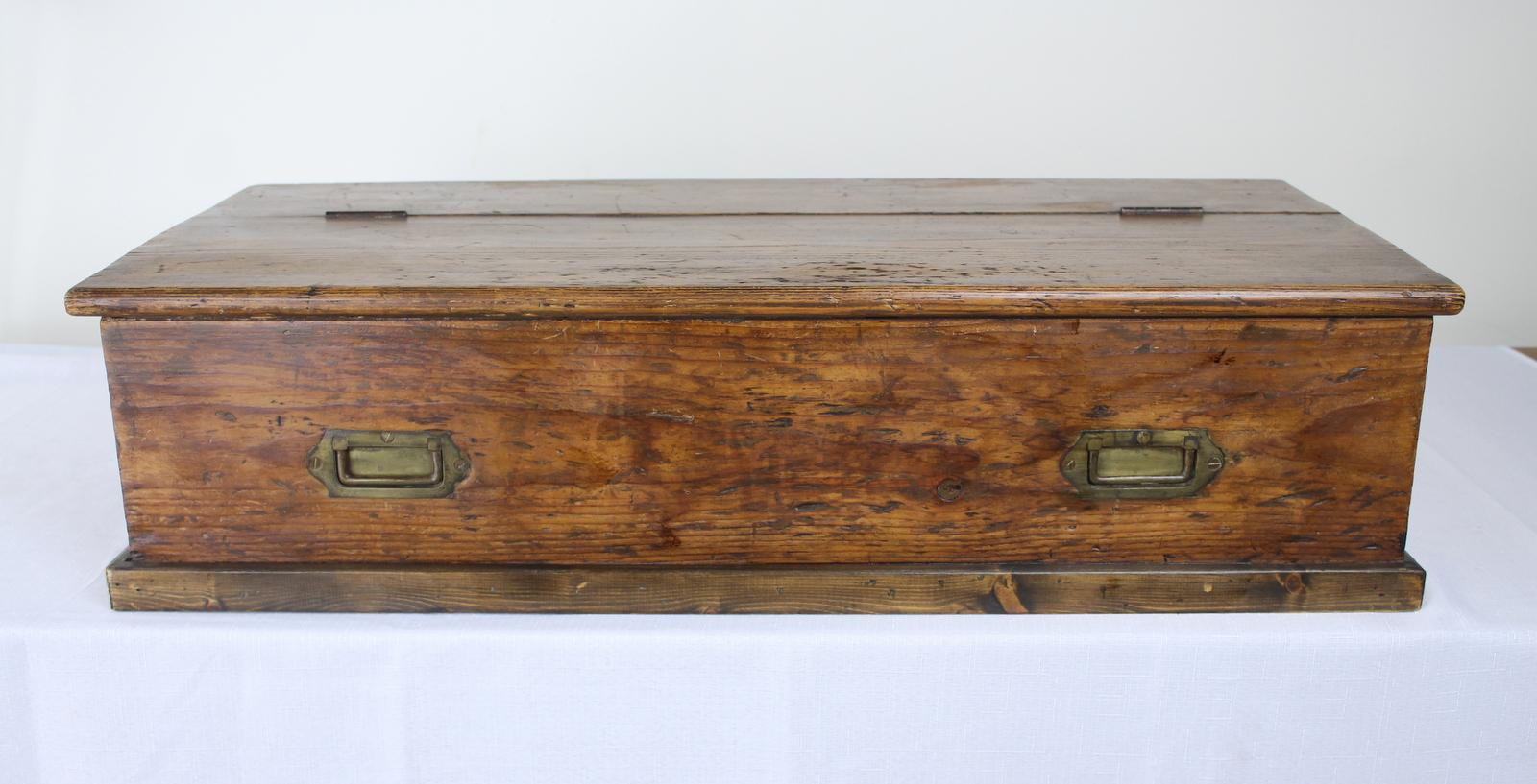 A simple pine British Campaign box with traditional drop handles to the front and sides. Top lifts at the center for roomy storage. Would look right at the base of a single bed.