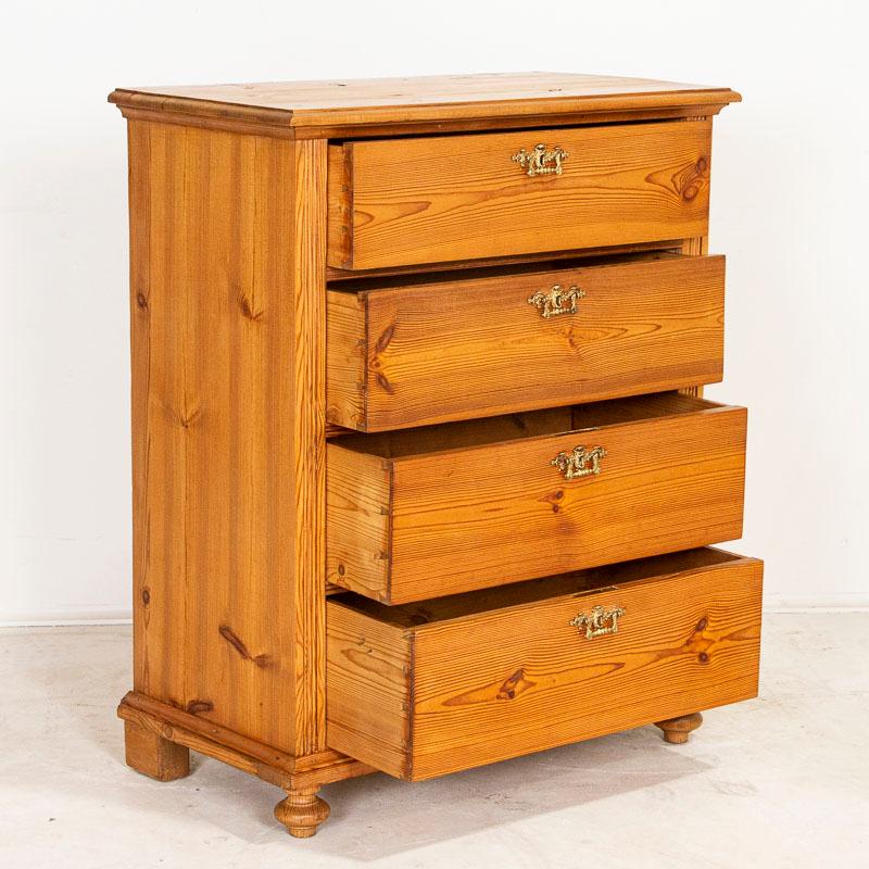 This antique pine chest of drawers has 4 drawers, providing ideal storage in a narrow space and stands at almost 3.5' tall. The simple carving along the sides, bun feet and dovetail joints were traditional style elements in furniture crafted in the