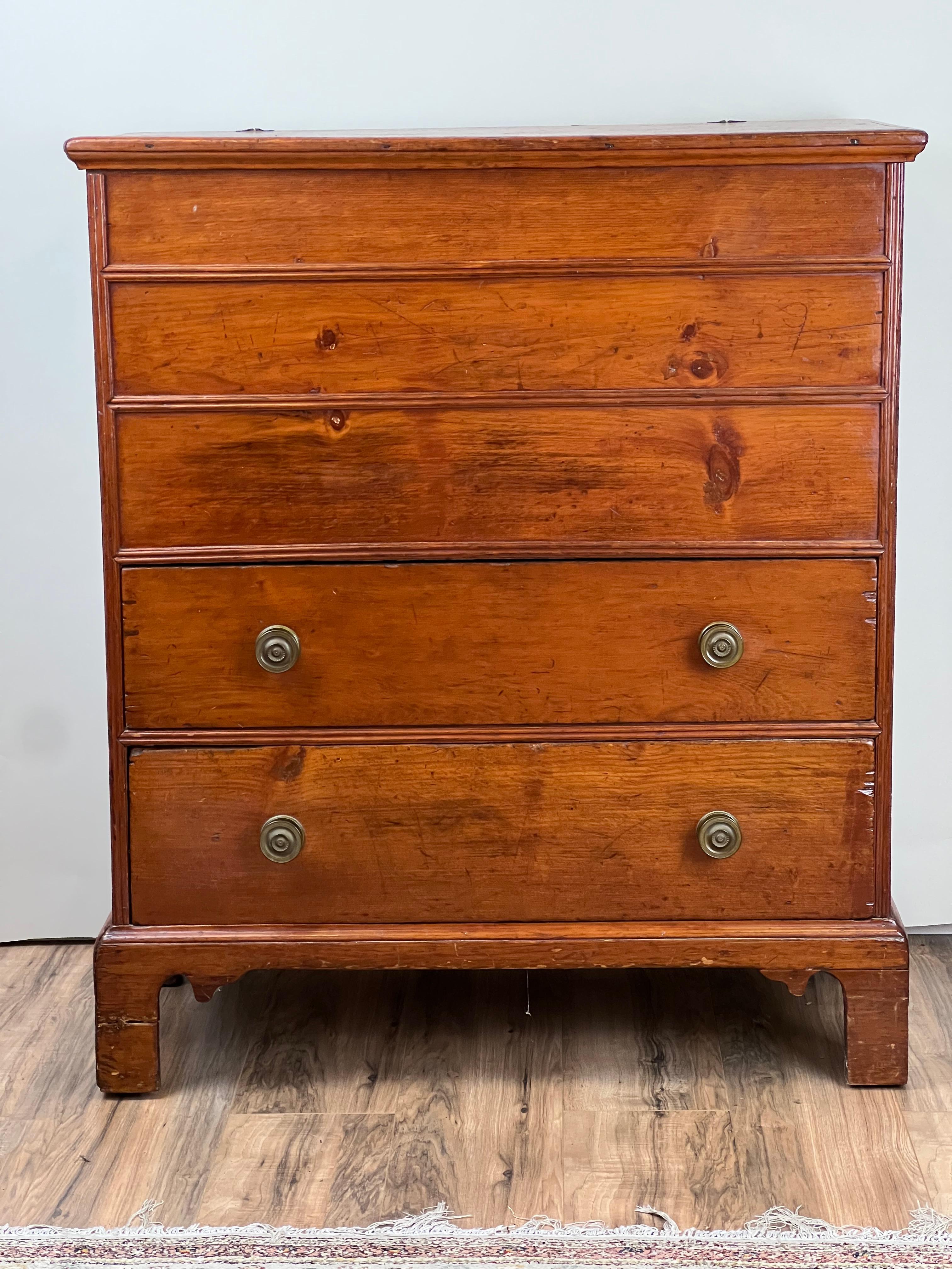 This charming late 18th-century pine blanket chest reflects the straightforward craftsmanship and honest beauty of early American Chippendale furniture. The design, with its clean lines, molded edges, and bracket feet, captures the understated