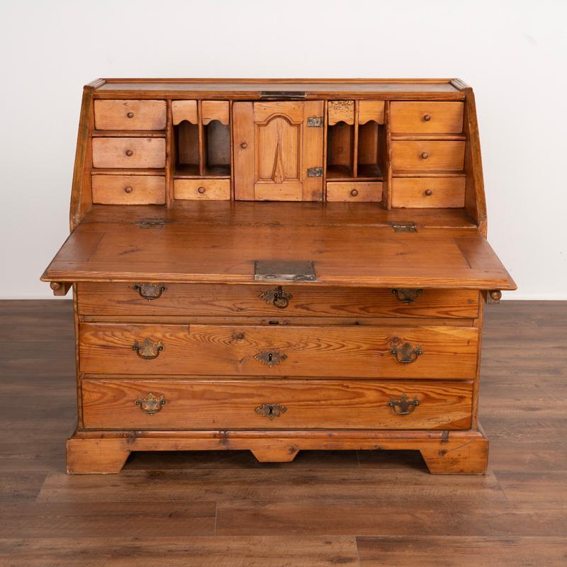 This drop front secretary is charming in every way, with a soft, satin wax finish that compliments the deeply aged patina of the pine and European country styling. The interior 12 drawers and one central cubbie with petite door create an inviting