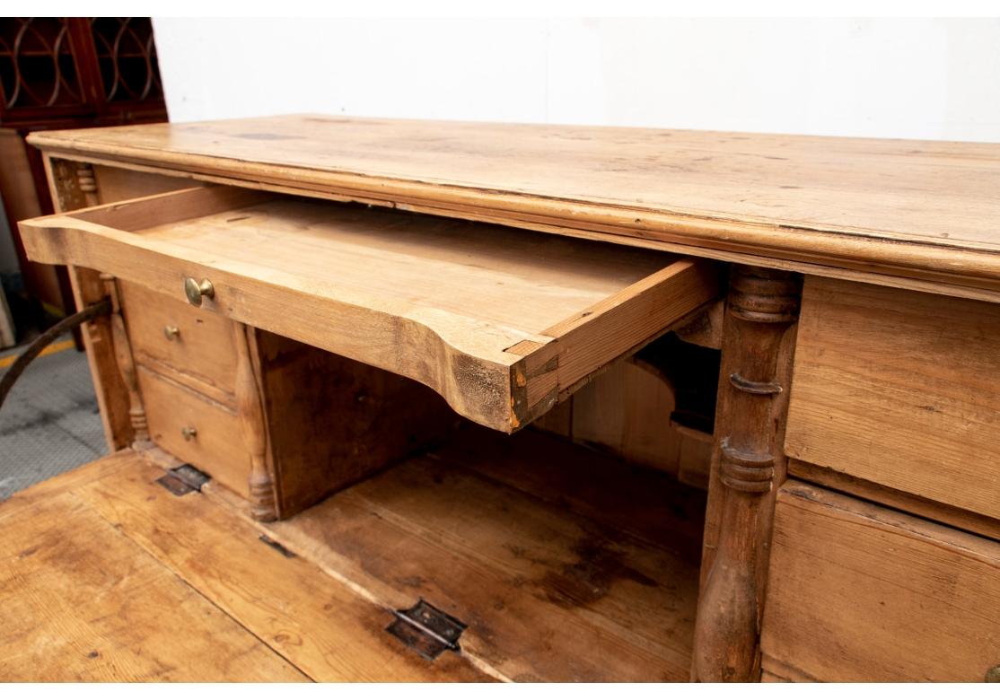 A tall cabinet with a banded drop front opening to seven drawers and a center open shelf flanked by turned balusters in relief.  The lower case with double doors and a single shelf inside. Raised on a skirt rail with bracket feet. The drop front and