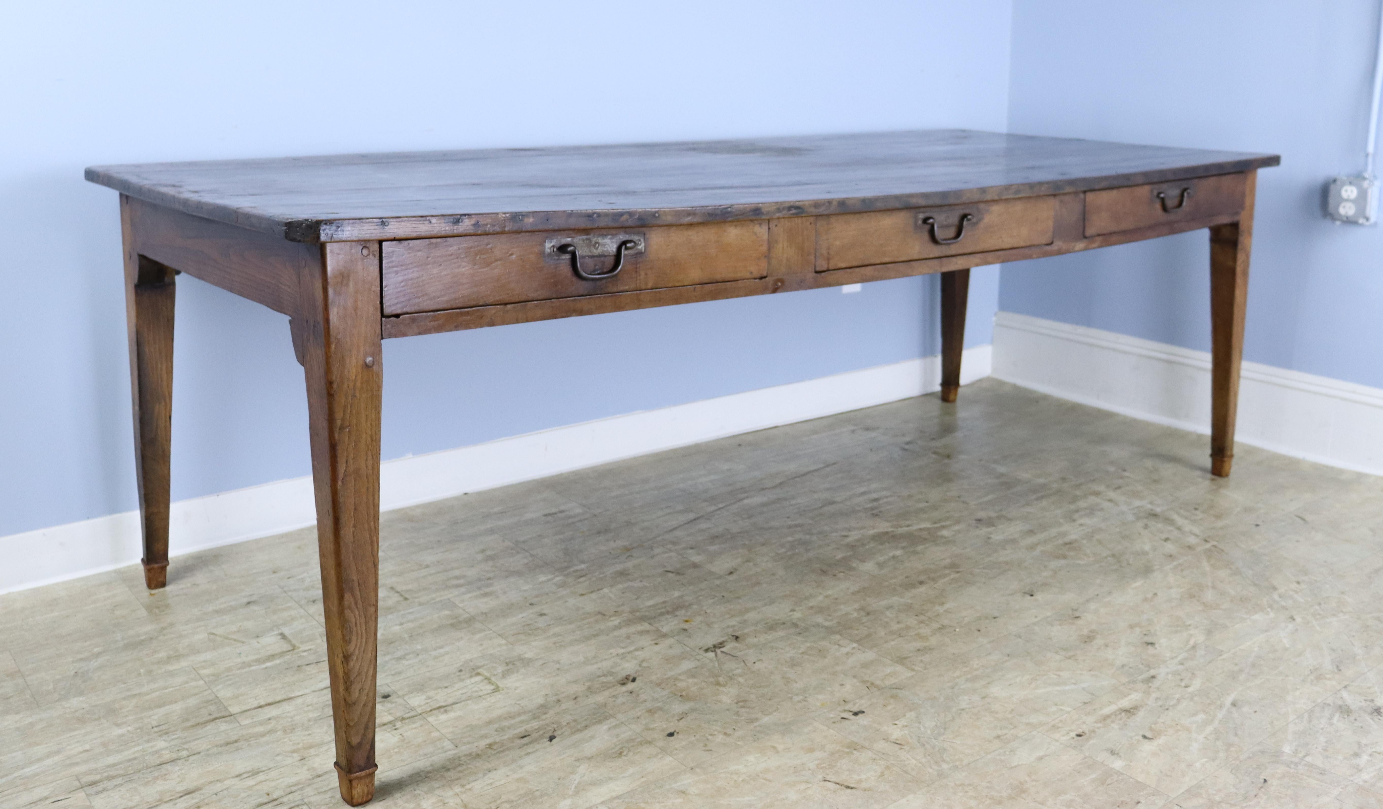A classic dark pine farm table with three deep drawers in the apron. The table top is in good condition with nice color and patina. Iron drop handles are replaced. Apron height of 23.5 inches is good for knees and there are 84 inches between the