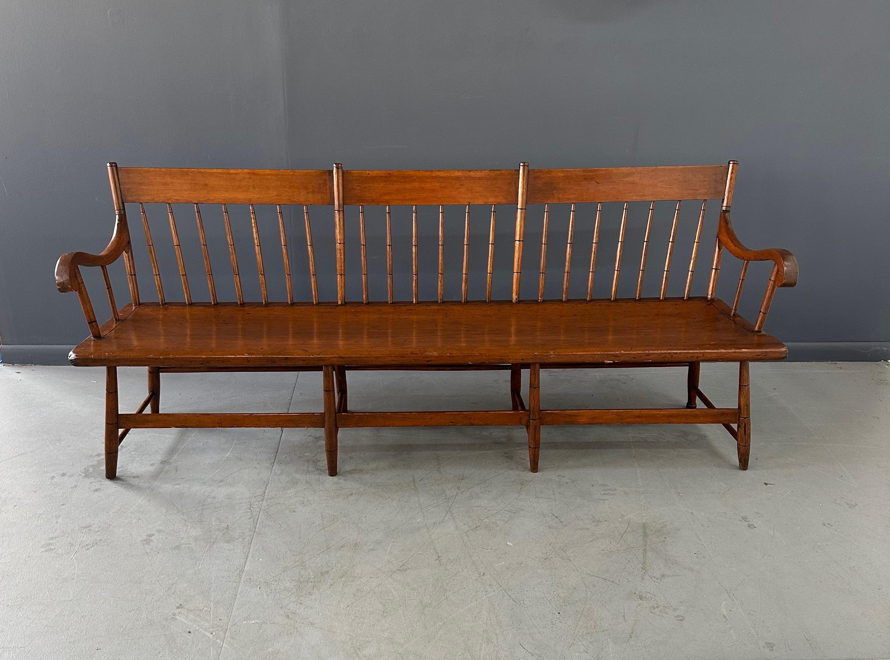 Crafted from pine, this antique Deacon's bench boasts a rustic aesthetic with its spindle back design. Its long size makes it perfect for use as a statement piece in a foyer or mudroom. Elevate your home decor with this beautifully handcrafted