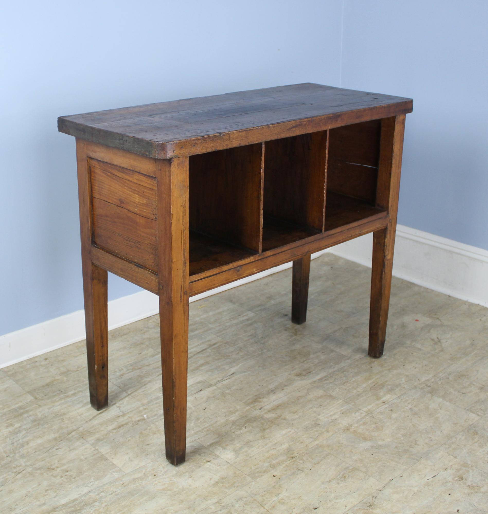 A rustic shelving unit on tapered legs in dark pine. Could serve a variety of purposes, from organizing trays to magazines to office supplies. Two small cracks in back, visible in image 3, to be expected in a piece of this age.  The individual