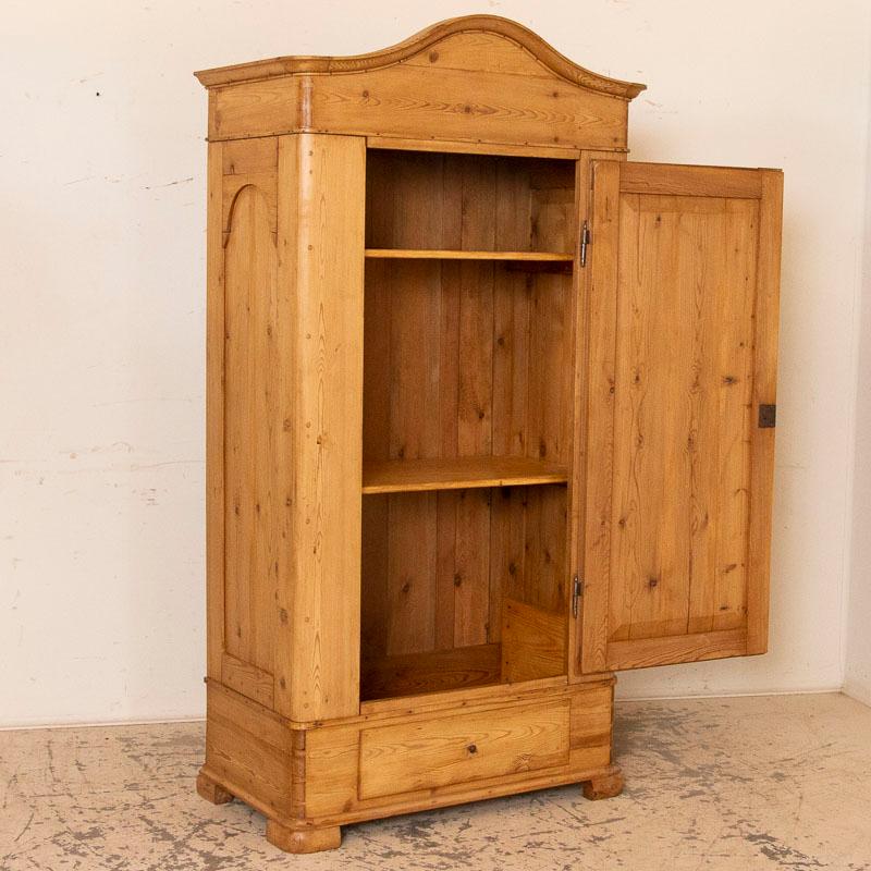 It is the beauty of the warm, aged wood that captures your attention in this pine armoire that stands almost 6 1/2ft tall. The lovely curves of the panels and bonnet add a touch of grace while the large dovetail joints and hardware remind us of its