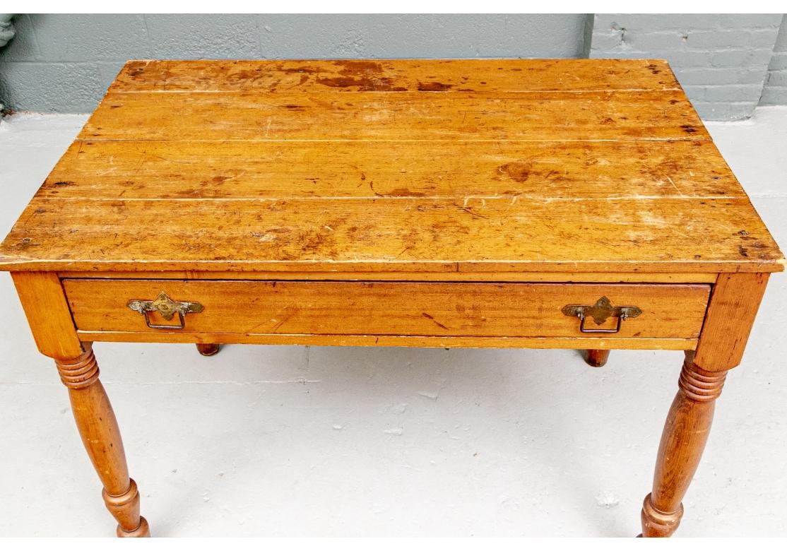 Table ou bureau ancien en pin avec plateau en planches, comportant un seul tiroir avec quincaillerie en fer et reposant sur un beau plateau en bois. 
les jambes tournées en anneau.
Dimensions : 43