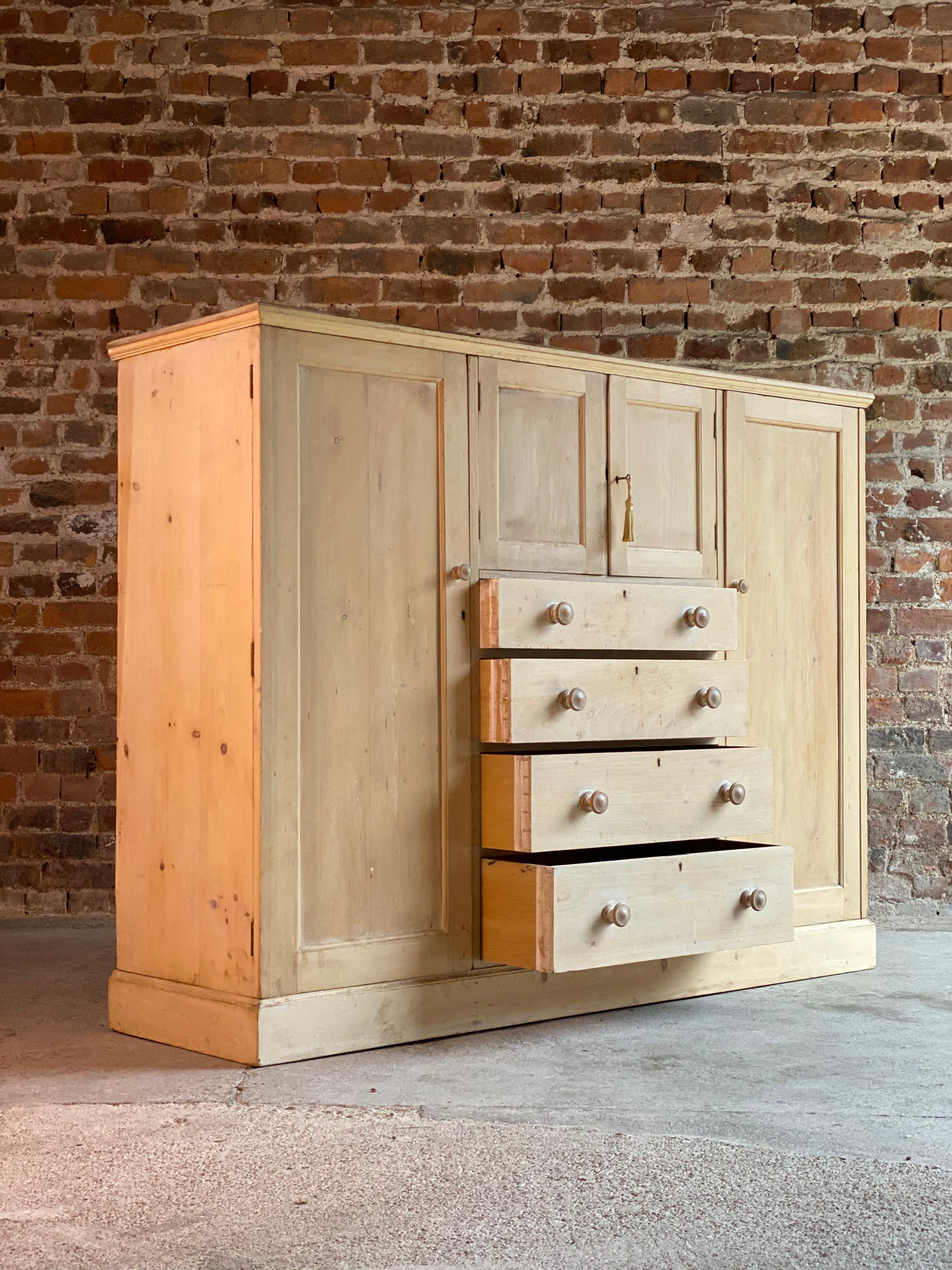 Fabulous 19th century stripped pine low wardrobe, the moulded top above two central panel doors over four long drawers with knob handles flanked by two panel doors enclosing shelved interior, with various hanging hooks, the cupboard to the right