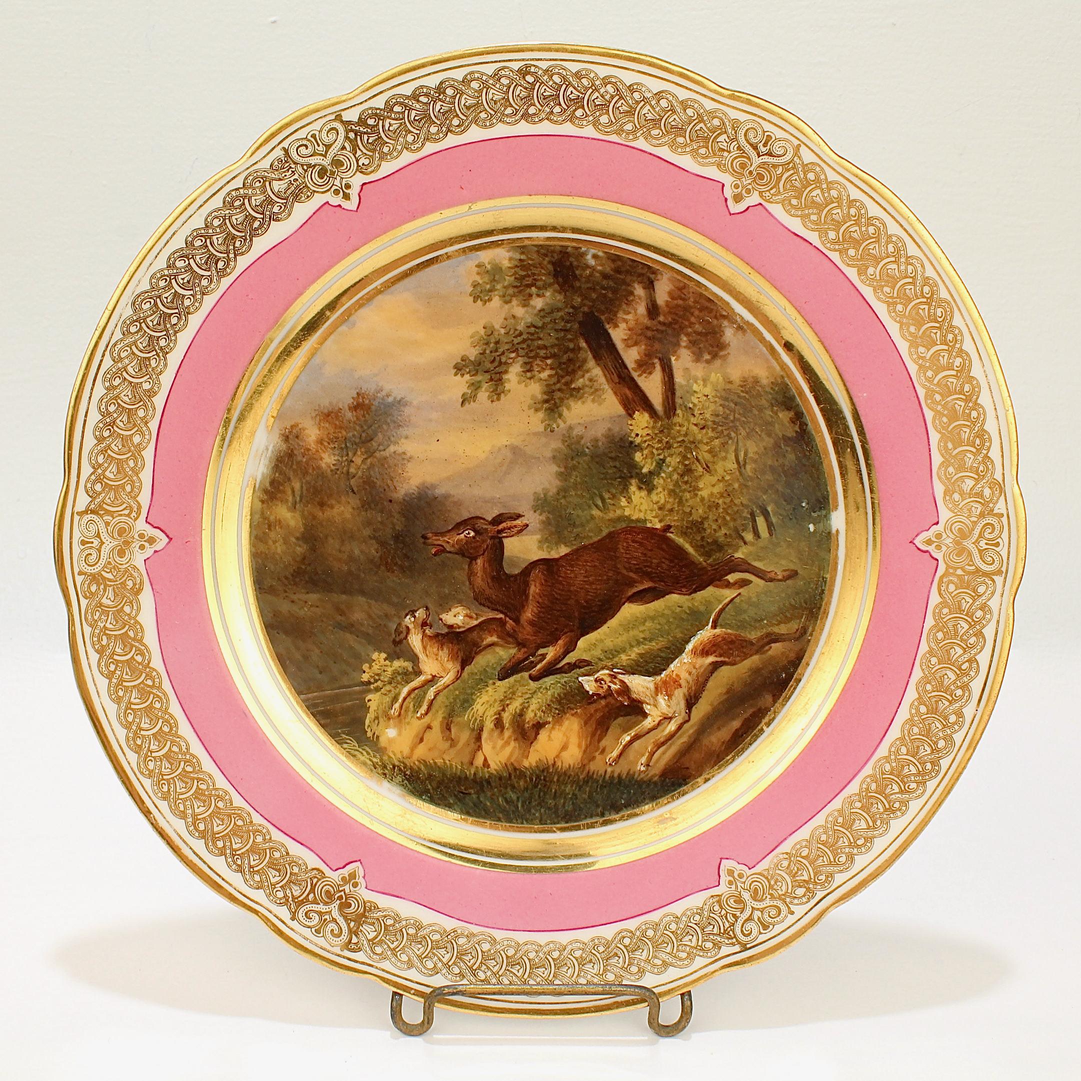 A wonderful antique 19th century Paris porcelain plate.

With a hand painted scene of a hunt scene in a bucolic landscape including a doe and 3 hounds giving chase. 

It has a rich pink border and an elaborate gilt design to the rim and a
