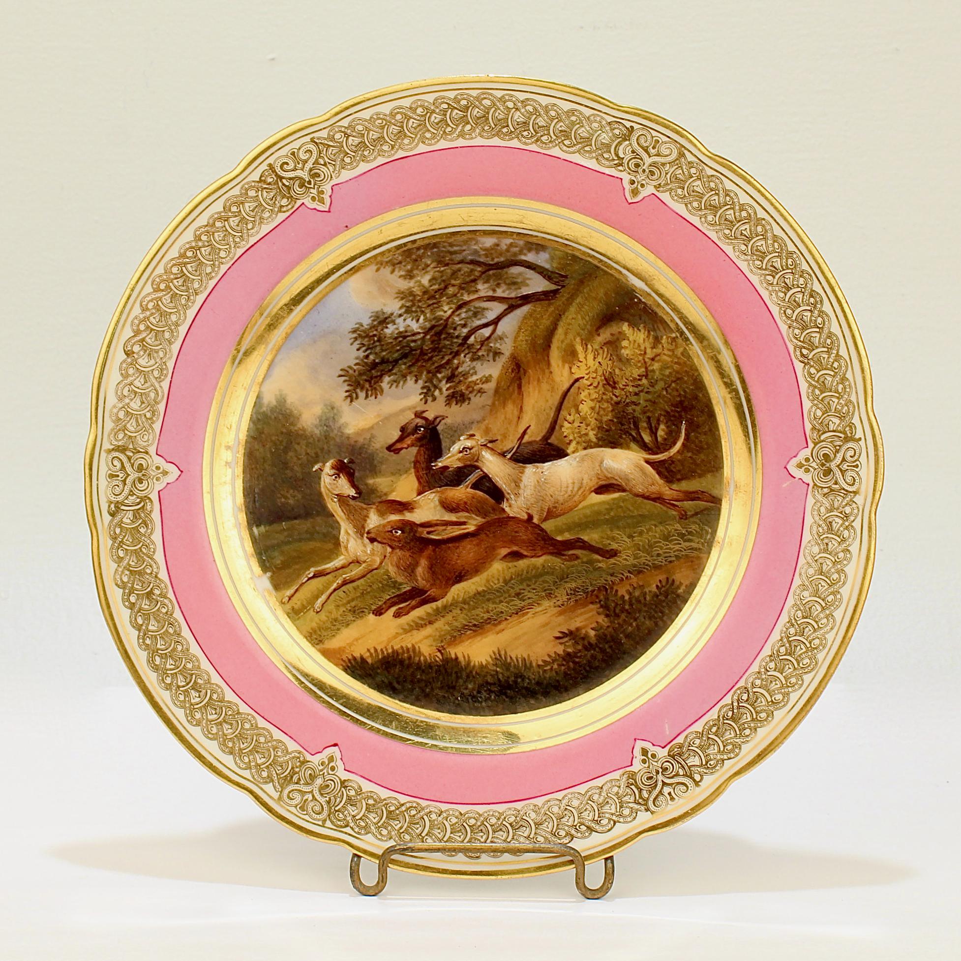 A wonderful antique 19th century Paris porcelain plate.

With a hand painted scene of a rabbit hunt in a bucolic landscape. Three greyhounds or whippets are giving chase.

It has a rich pink border and an elaborate gilt design to the rim and a