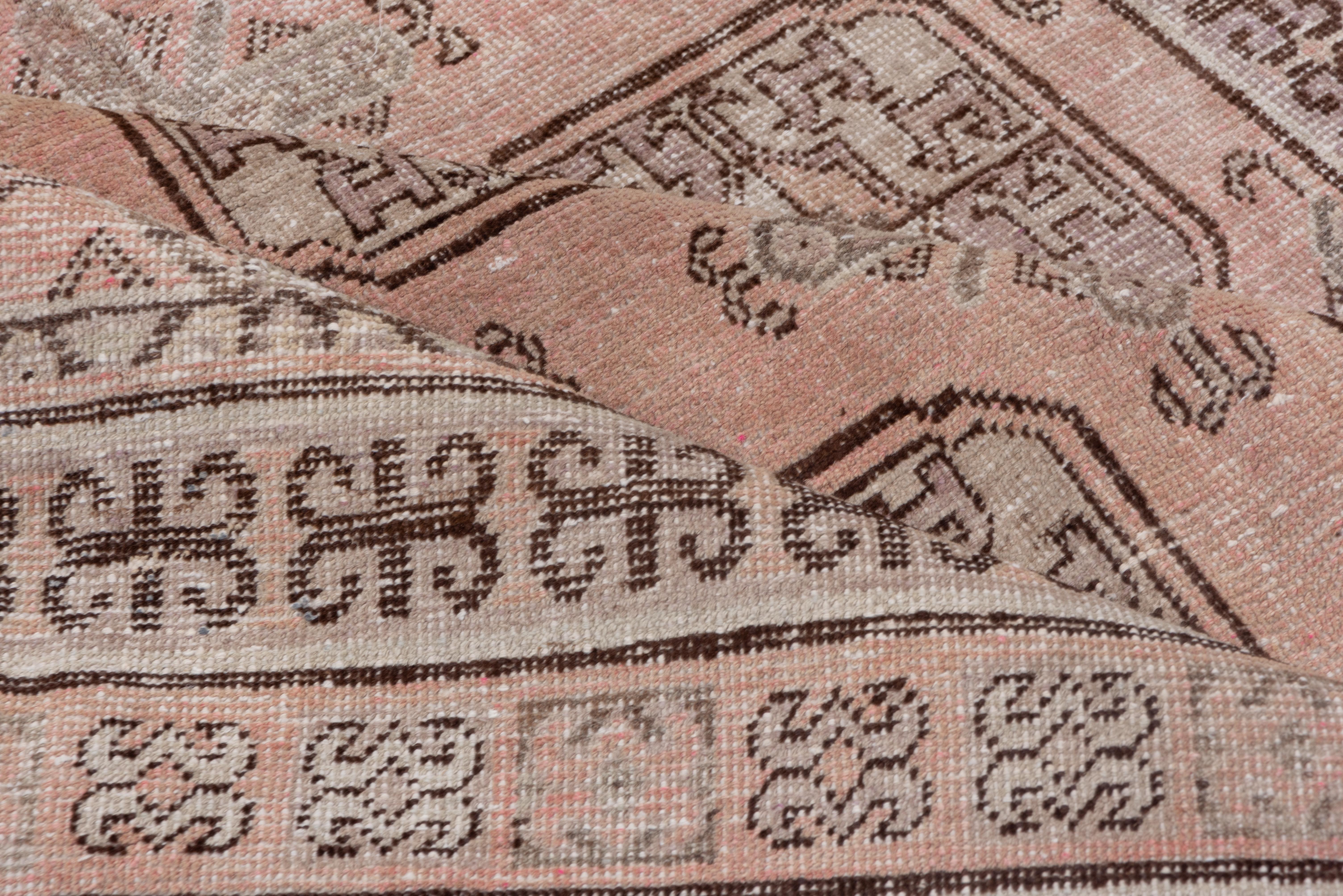 This east Turkestan town carpet shows a four-column layout of octagonal Turkmen-style Tauk Noska guls with chemche minor guls between on a straw-pink ground, set within double ram's Horn and other repeating Turkmen nomadic style borders.