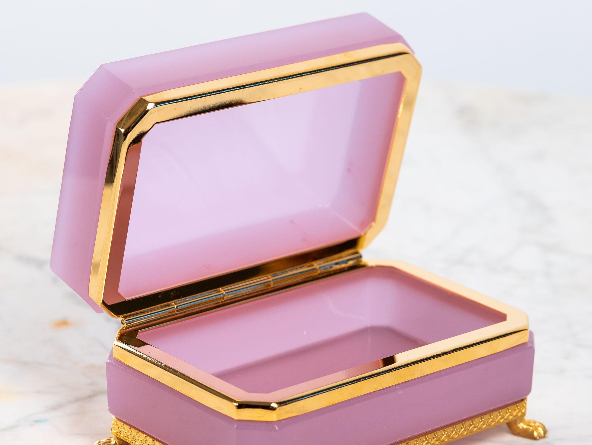 An antique French opaline glass casket box in a striking pale pink color. The polished glass is mounted with finely detailed gold bronze hardware and feet, adding elegance to the vibrant hue. The glass color and feet mounts are rare and highly