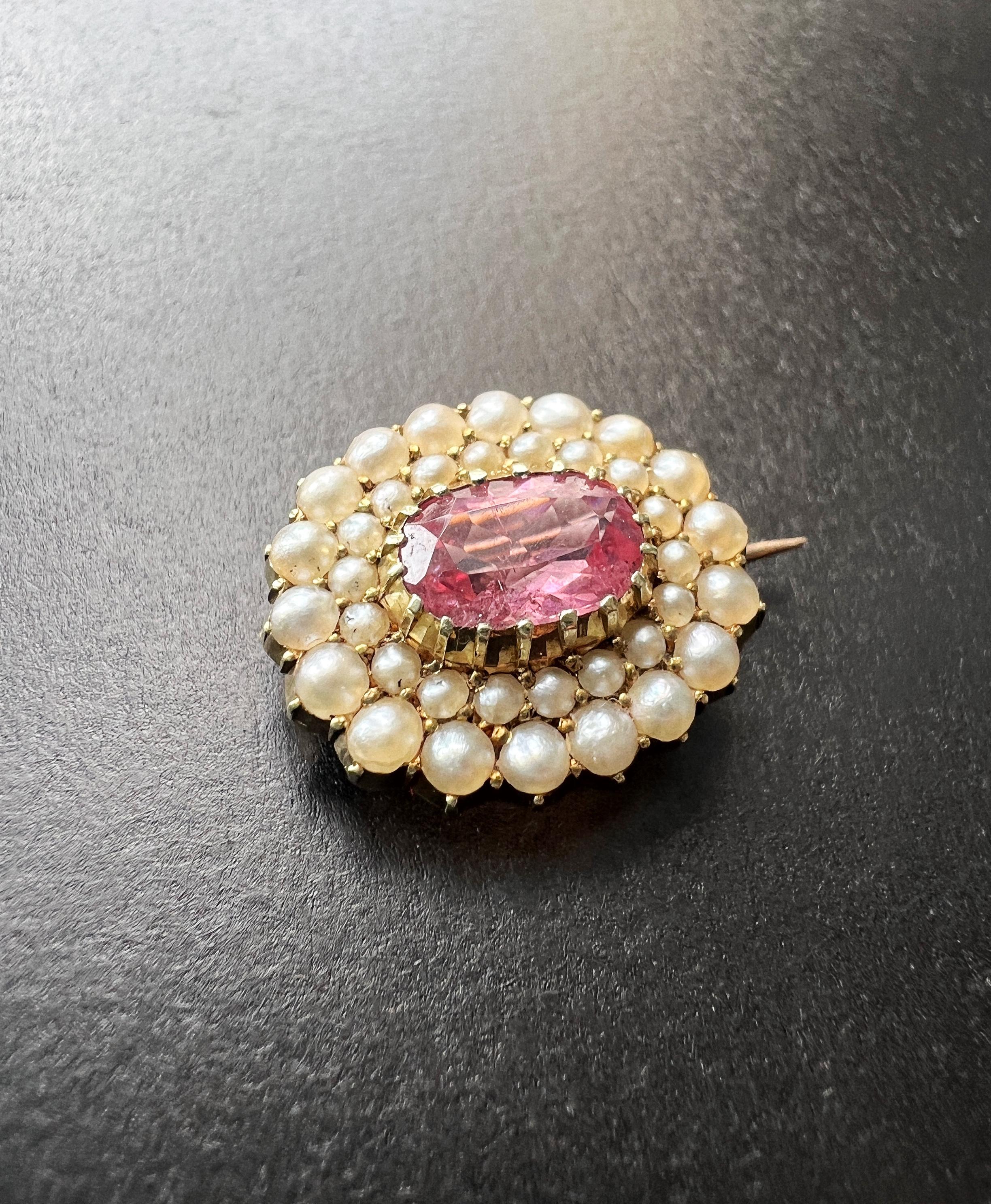 This stunning early 19th century (Early Victorian era) brooch features a vivid pink tourmaline as its centerpiece. The gemstone measures 9mm in length and 6.5mm in width. It is cushion cut, open backed and prong set in the center of the brooch,