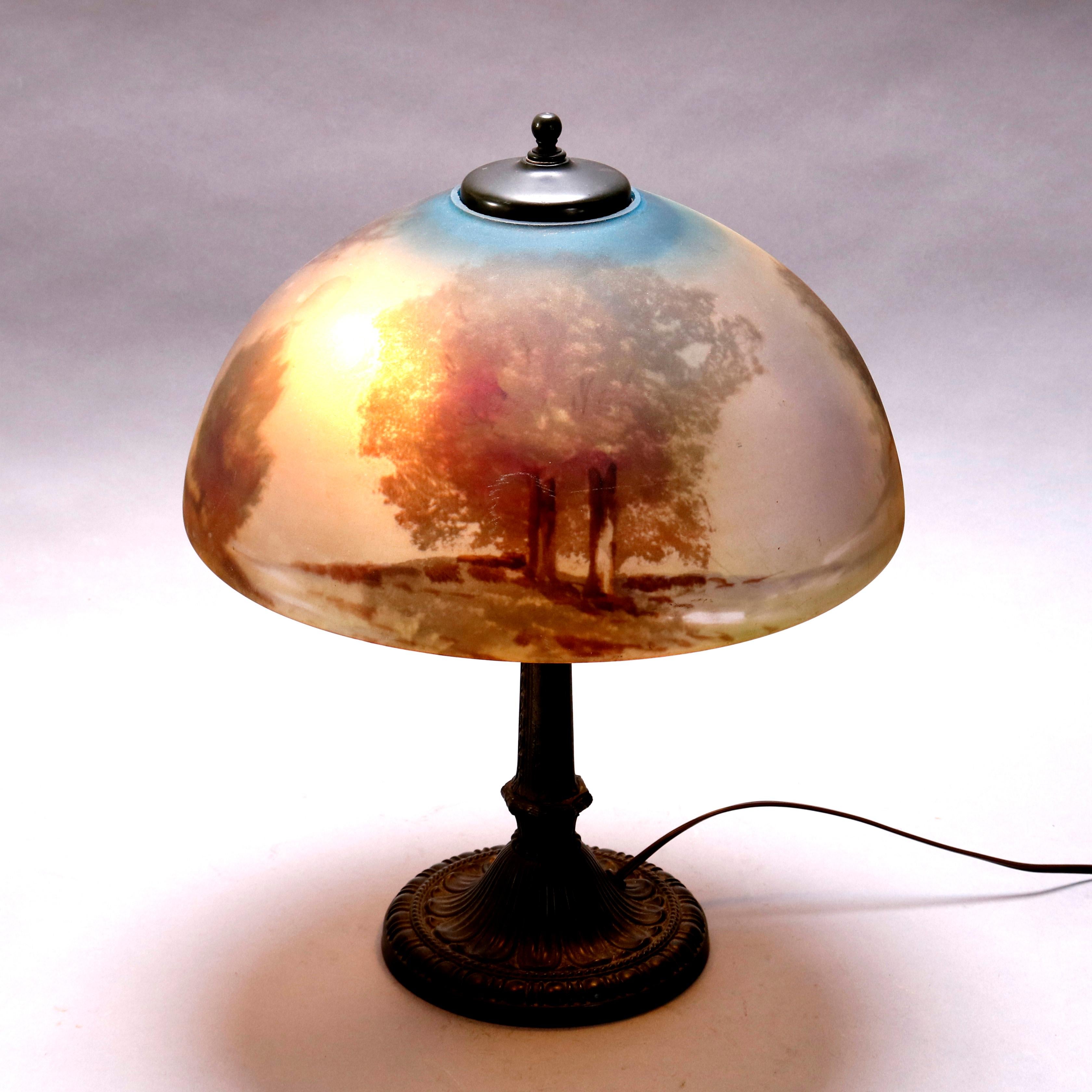 An antique Arts & Crafts Pittsburgh School table lamp by E. Miller & Co. offers cast bronze base having Dual independently controlled sockets, is embossed with maker, and surmounted by a reverse painted glass dome form shade with cottage in woodland