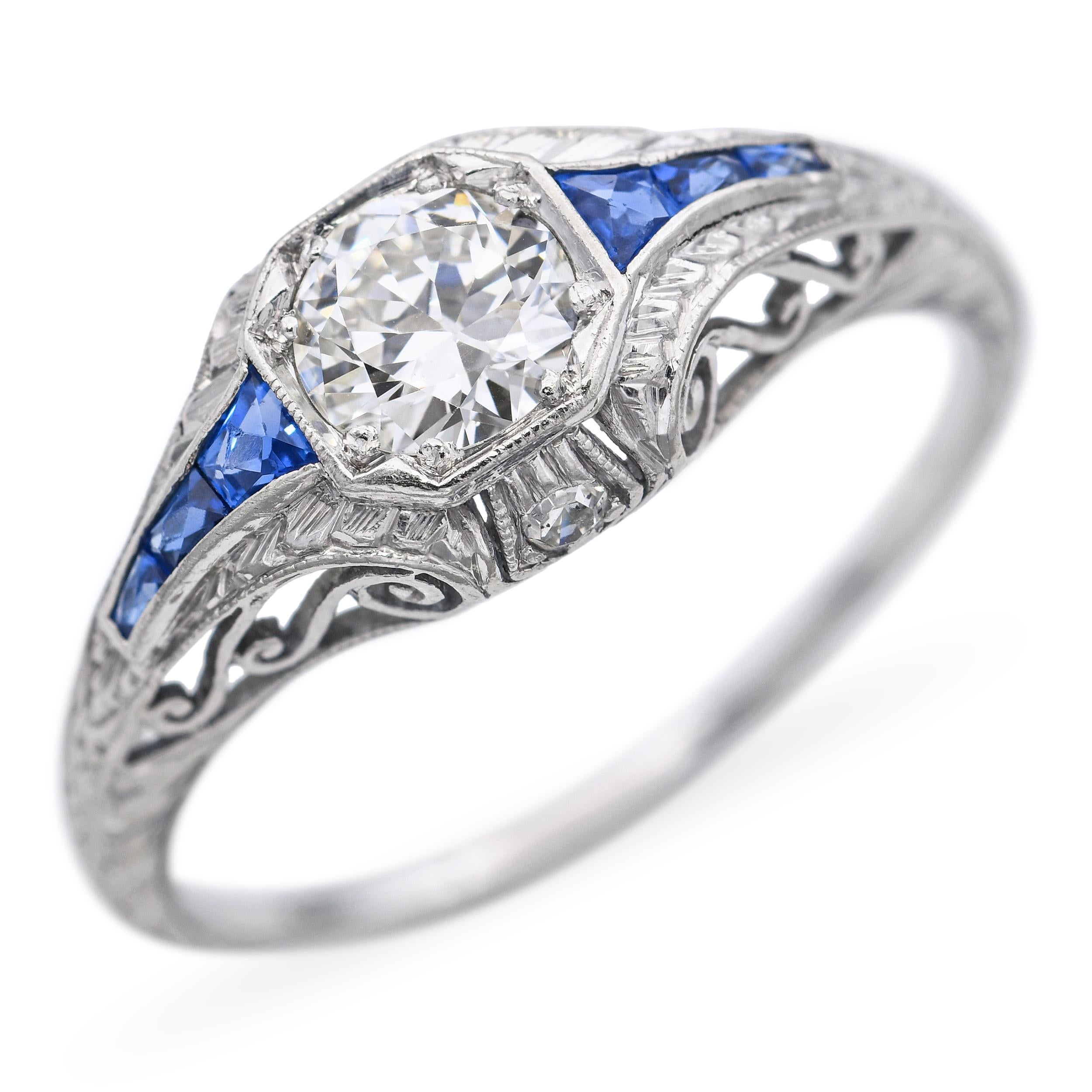 Este elegante anillo de compromiso antiguo está elaborado en platino atemporal y presenta un brillante diamante central de 0,52 quilates, bellamente acentuado por vibrantes zafiros azules que enmarcan la piedra con rico contraste y encanto vintage.