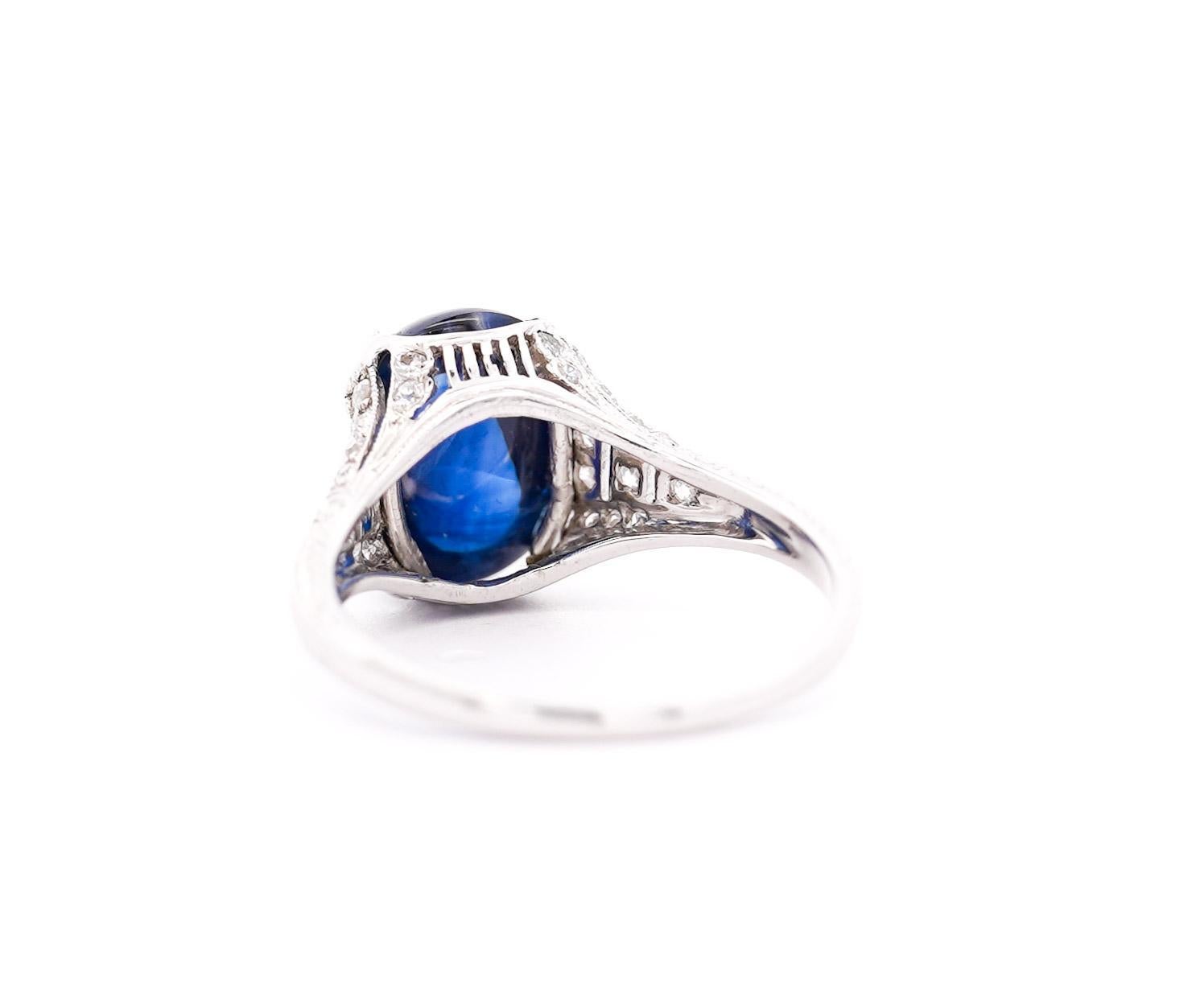 A mesmerizing 5.50 carat cabochon sapphire from Sri Lanka shimmers at the heart of this Art Deco masterpiece in a stunning prong and halo setting. Crafted in platinum, its intricate filigree echoes the era's glamour, while 32 diamonds add a touch of