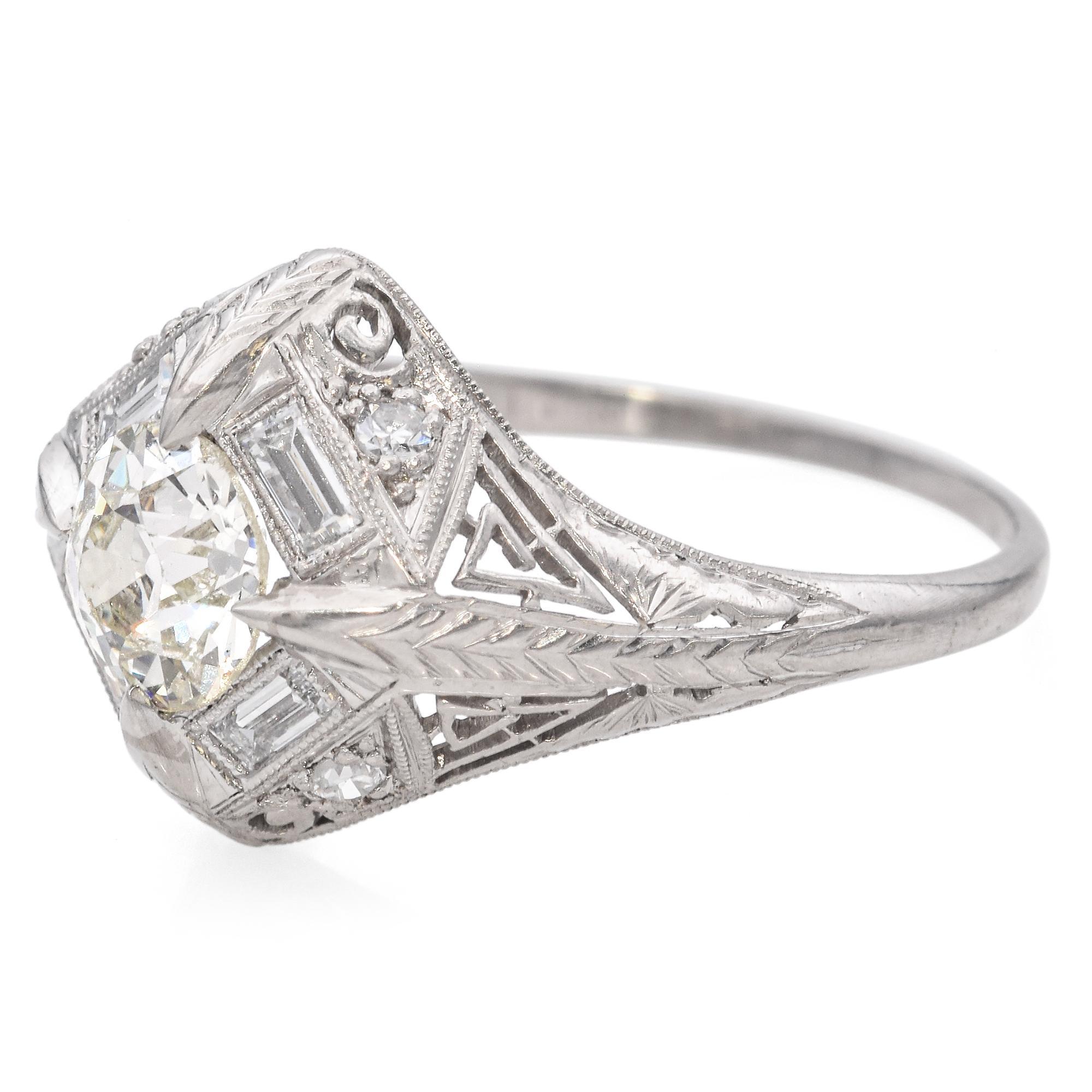 Expertly crafted in platinum, this exquisite ring showcases a central round brilliant-cut diamond, surrounded by a geometric arrangement of baguette-cut diamonds. The intricate filigree detailing enhances the elegance of the design, with delicate