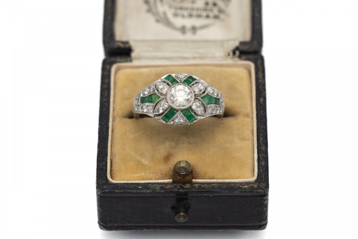 Antique platinum ring in the Art Deco style.

Decorated with a central diamond weighing 0.50ct and additional 28 diamonds weighing 0.35ct and emeralds with a total weight of 0.50ct.

It comes from the 1930s-1940s Hungary.

Very good condition, no