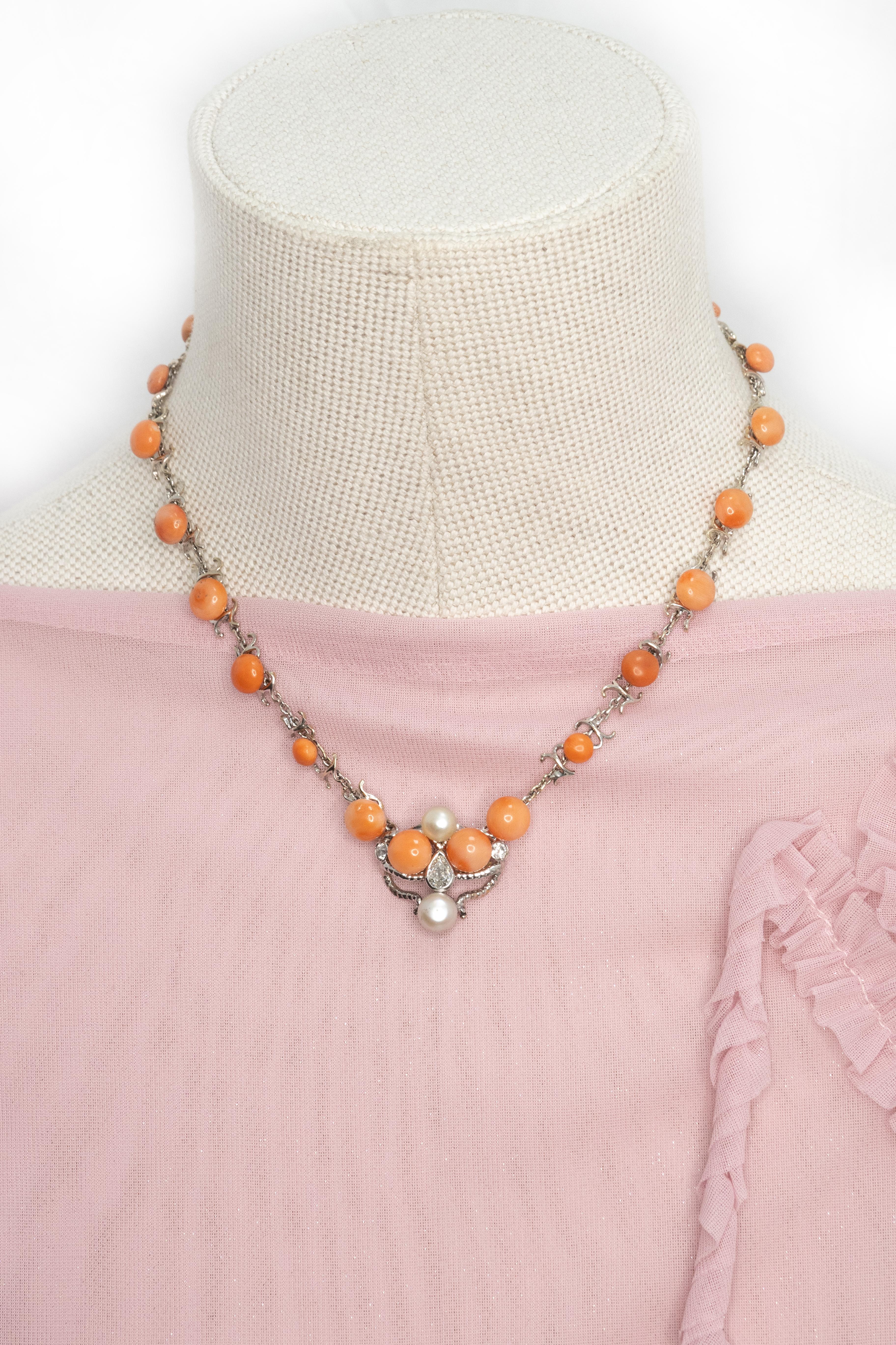 Una raffinata collana antica realizzata in platino, che mostra vibranti perle di corallo color salmone elegantemente collegate con connettori decorativi traforati. Il centro è caratterizzato da un grazioso motivo simmetrico con tre perle color
