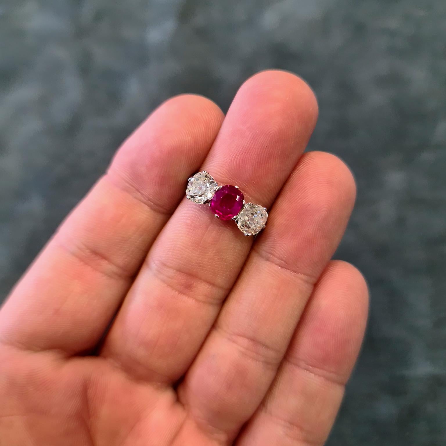 An exquisite early 20th century platinum three stone ring, featuring a central blood-red, unheated Burma ruby of approximately 1.10 carat, flanked on either side by an old-cut diamond. Total diamond carat weight of approximately 2.50 carats, H-I