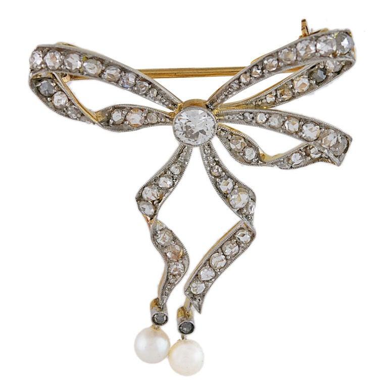 Graceful antique figural bow pin. Platinum and 18K gold, entrusted with rose diamonds. Center stone is a full cut diamond approx..45cts.Suspended with two pearls