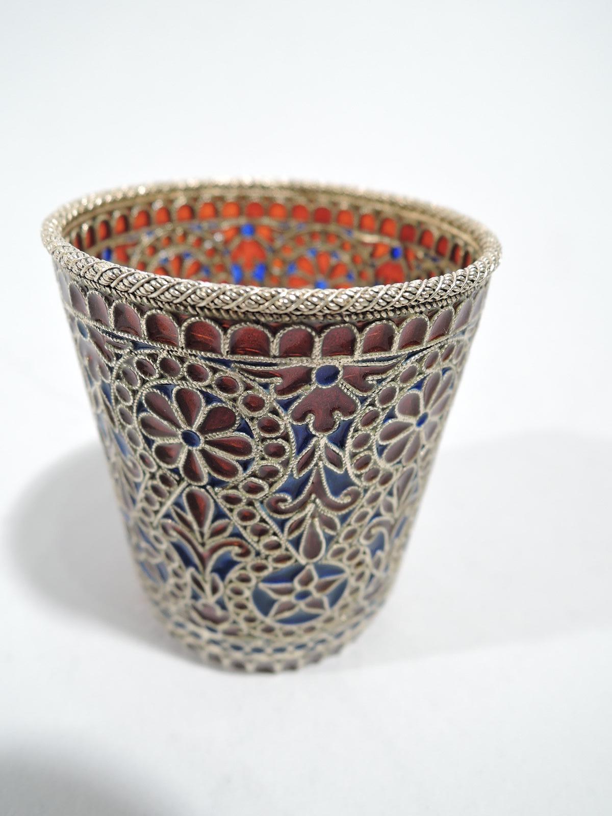 Richly colored plique a jour beaker, ca 1910. Straight and gently tapering sides. Ornament includes stylized flower heads in rondels and beaded and guilloche borders. Colors red and blue. Silver gilt wire frames and cabled rim. Unmarked.
