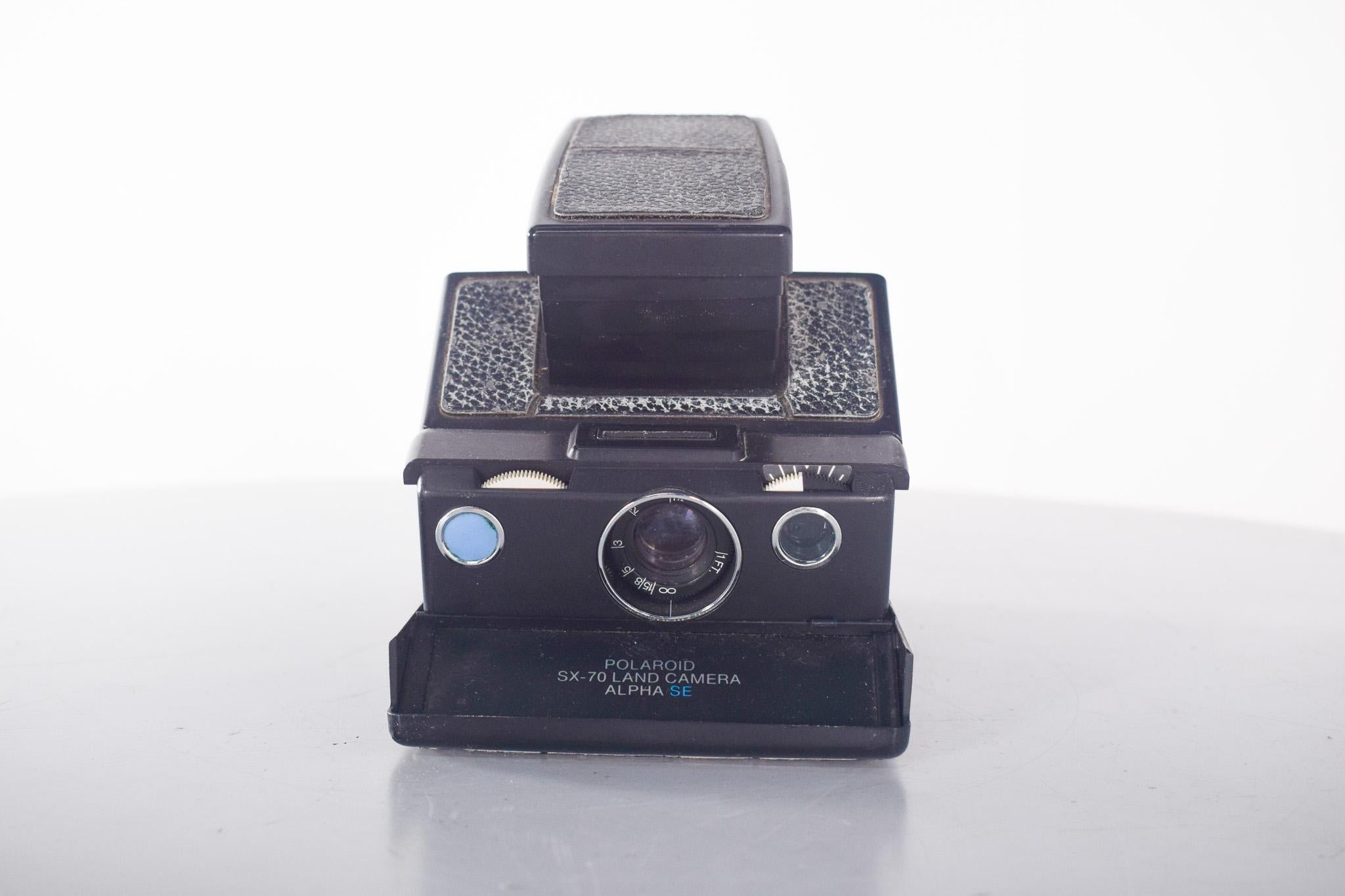 Appareil photo Polaroid, Alpha SE, SX 70. Produit par Polaroid à partir des années 1970. Ce modèle se distingue par son corps pliable en cuir et métal, présenté ici dans une élégante version noire texturée. Grâce à son fonctionnement instantané, il