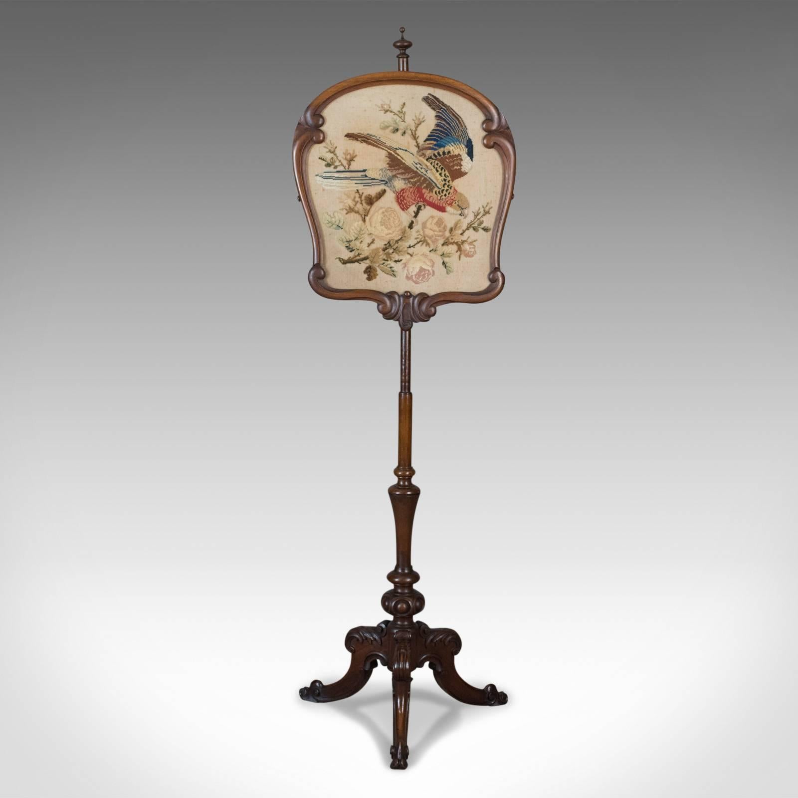 This is an antique pole screen, an English, early Victorian fire screen with needlepoint tapestry panel dating to circa 1850.

Raised on a turned mahogany Stand with good color and grain interest
A tripod of cabriole legs featuring carved 'C'