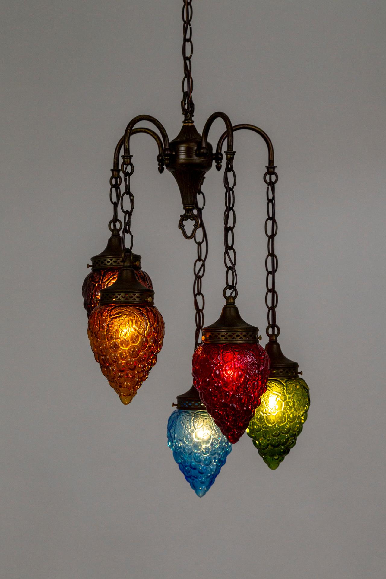 An early 20th-century light fixture comprised of 5 multicolored, pressed glass grape clusters with varied-length chains dangling from a sprouted center. The brass structure has a pleasing antique tone with cut details on the shade holders. The