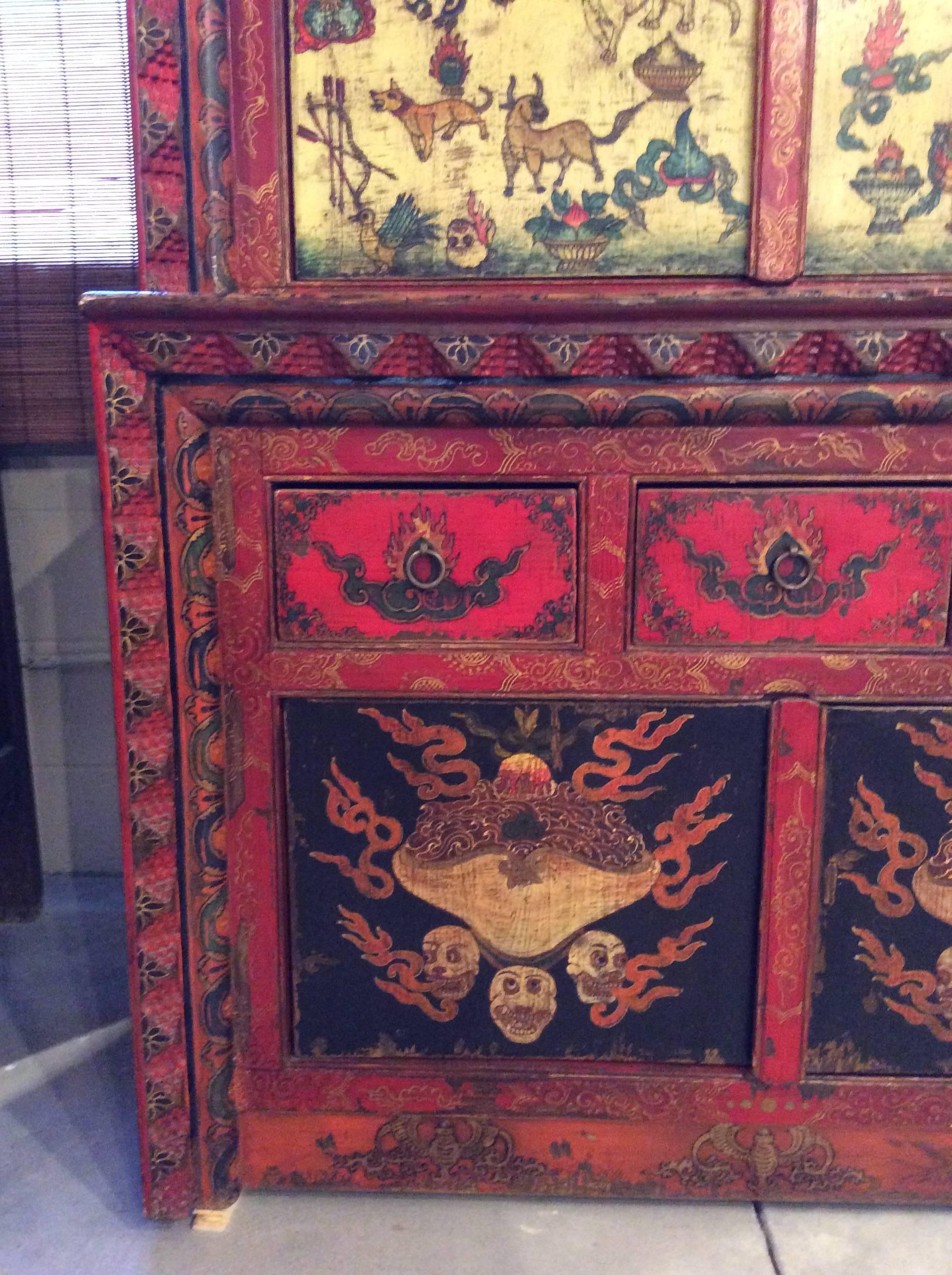 This antique cabinet is painted with a multitude of auspicious Tibetan Buddhist symbols, both decorative and figural.