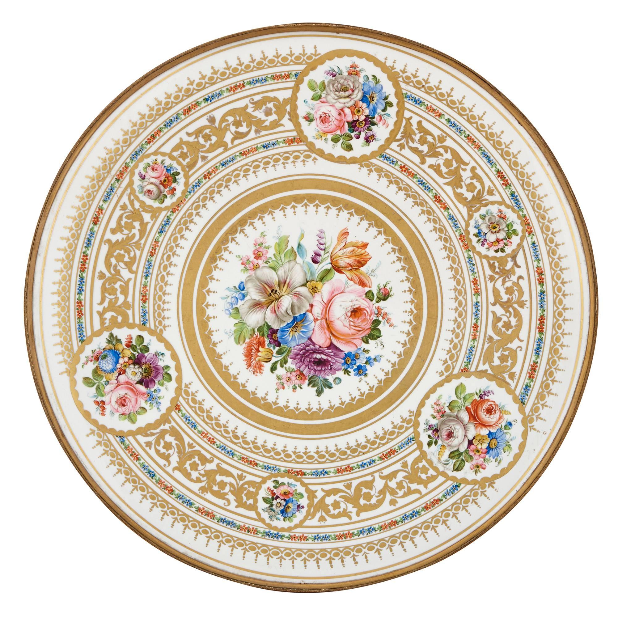 This delicately detailed circular gueridon table is crafted of ormolu, and features a very fine hand painted porcelain top. The porcelain top is decorated with flowers in circular patterns, set on a white ground with parcel gilt detailing. The edge