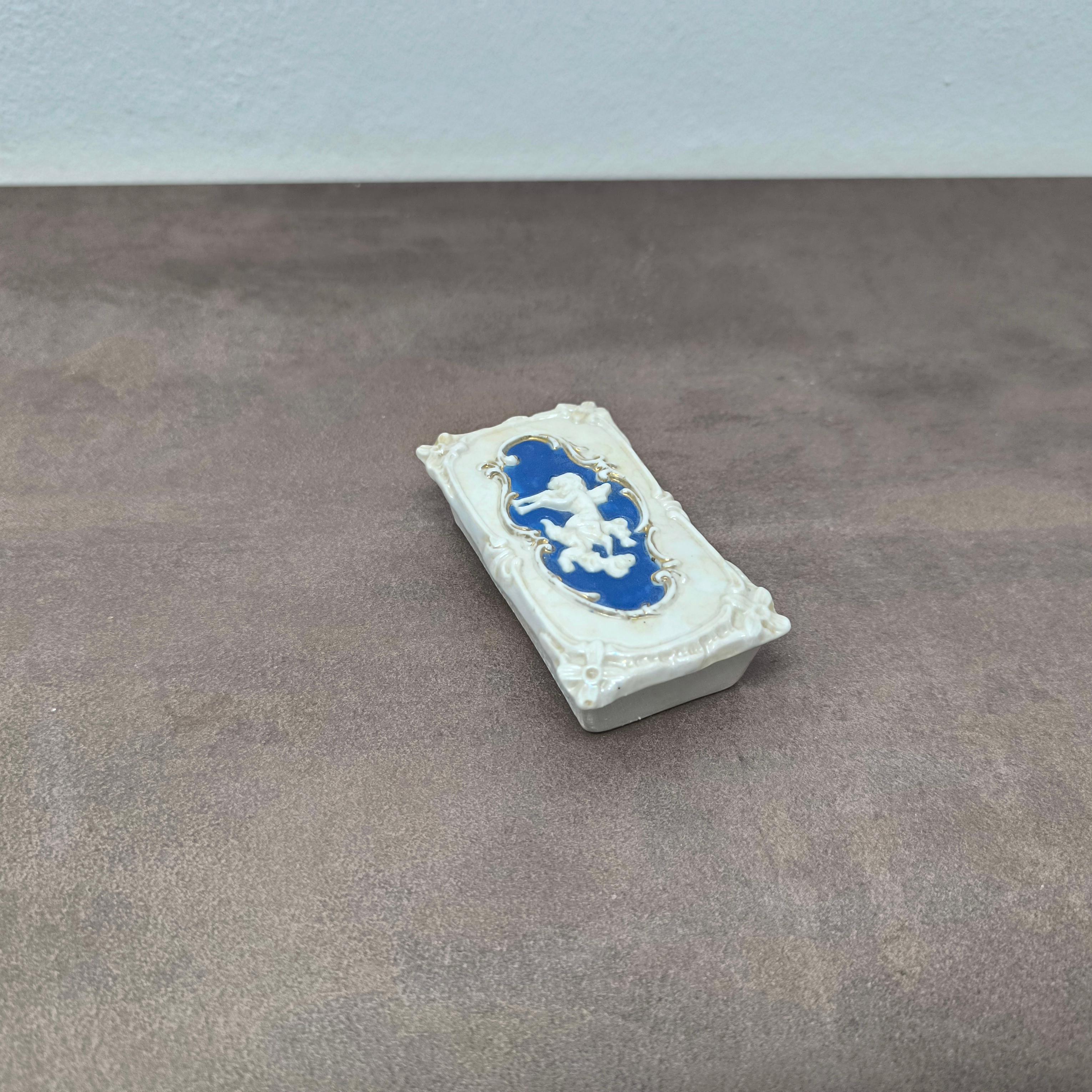 Ancienne boîte à chérubin en porcelaine avec couvercle en relief, c. Fin du 19e siècle
Dimensions : 20 × 5,5 × 3 cm
Boîte à bibelots ou de présentation en porcelaine finement moulée, présentant un chérubin ailé en relief sur un fond bleu tendre de