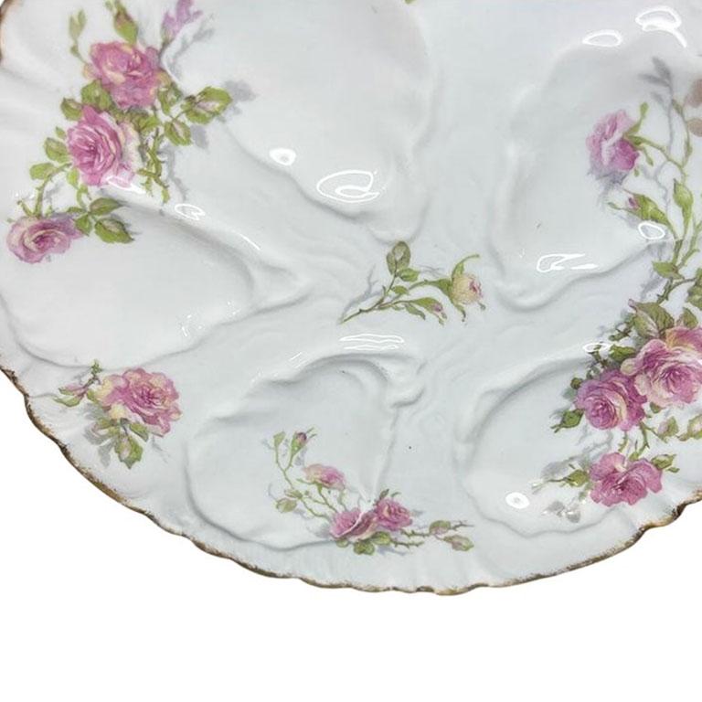 A round porcelain oyster plate with pink and green floral detail. This piece will be great in a grouping hung on a wall, or used as a dish to serve oysters! The plate is round and features five wells in the shape of oyster shells. (When used as a