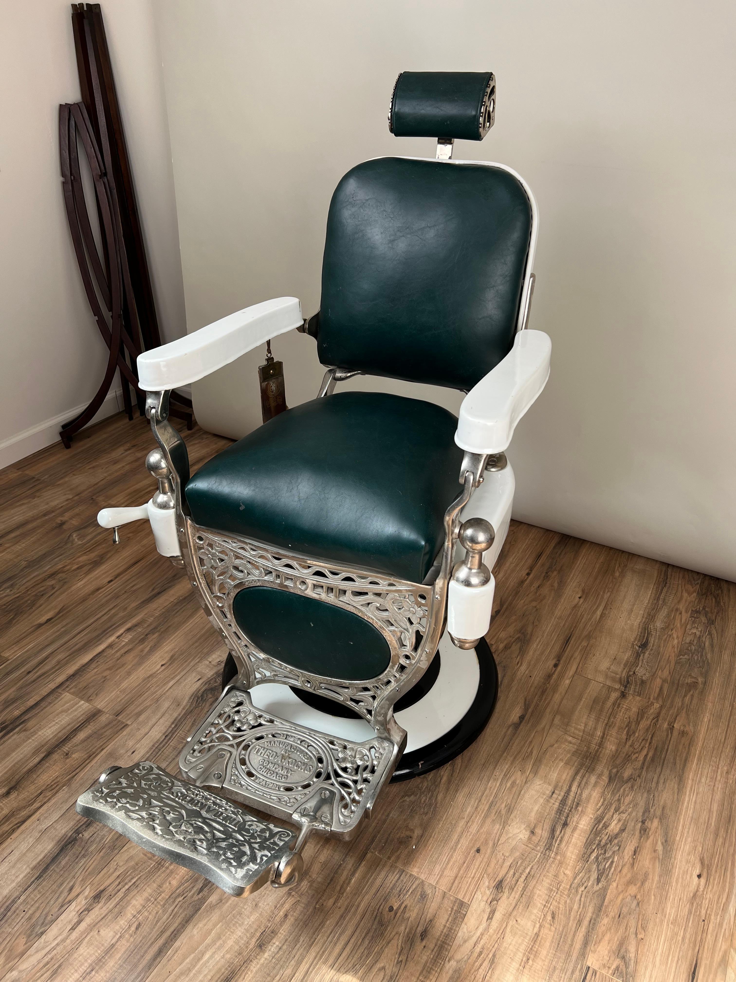 This Antique Porcelain Theo A. Kochs Chicago Barber Chair, dating to around 1920, is a striking example of early 20th-century craftsmanship and design. The chair features a robust porcelain frame with intricate detailing, showcasing the functional