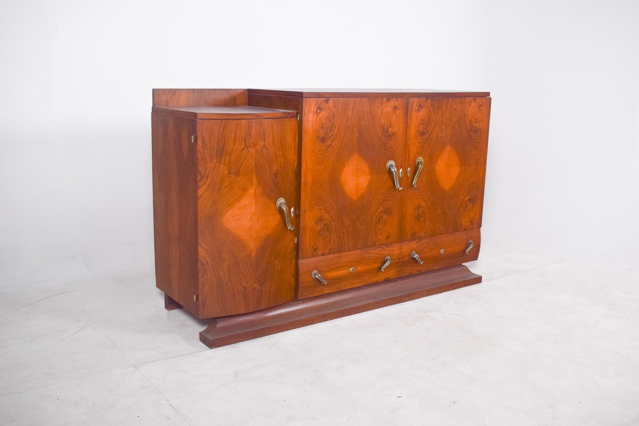 Buffet Art Déco. D'un design symétrique et équilibré, la pièce présente des portes recouvertes de placages de bois naturel dans un motif de marqueterie en miroir, qui forment des motifs géométriques et organiques dans les veines, créant un effet