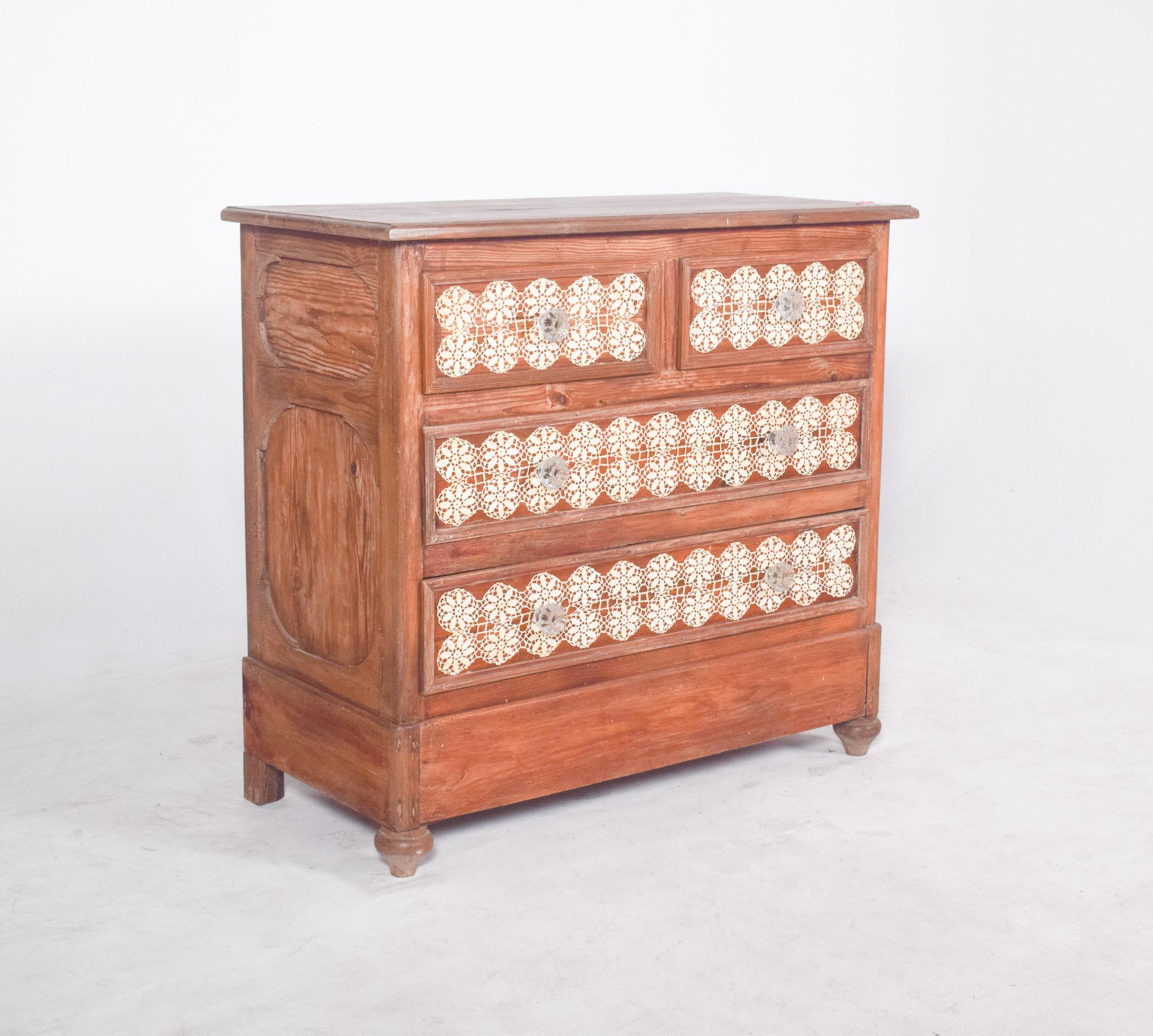 Chest of drawers with crochet. The body has a solid structure, finished in a natural colour with a slightly aged appearance, where the grain of the wood is evident. The sides are decorated with ovalised carved panels, adding relief and texture to
