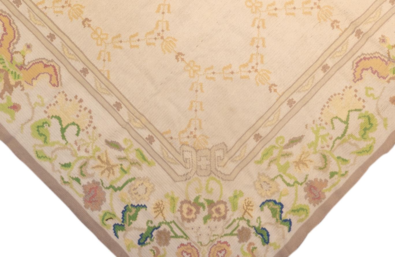 This oversize Continental Moderne needlepoint carpet has a creamy sand field supporting an open hexagonal yellow floral lattice. The sandy ivory major border shows ragged 