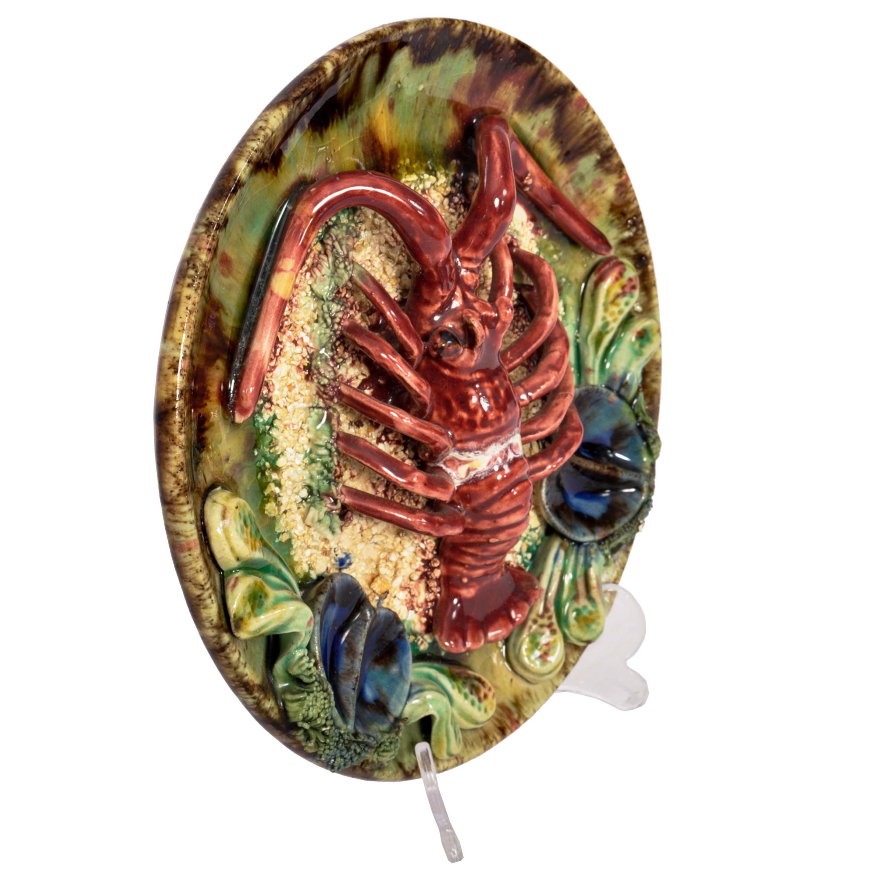 A good antique Palissy Ware style Portuguese majolica wall plate, circa 1900.
The plate decorated with a large lobster to the center resting on a textured ground and flanked by two sets of mussel shells. The plate having a a manganese glaze with