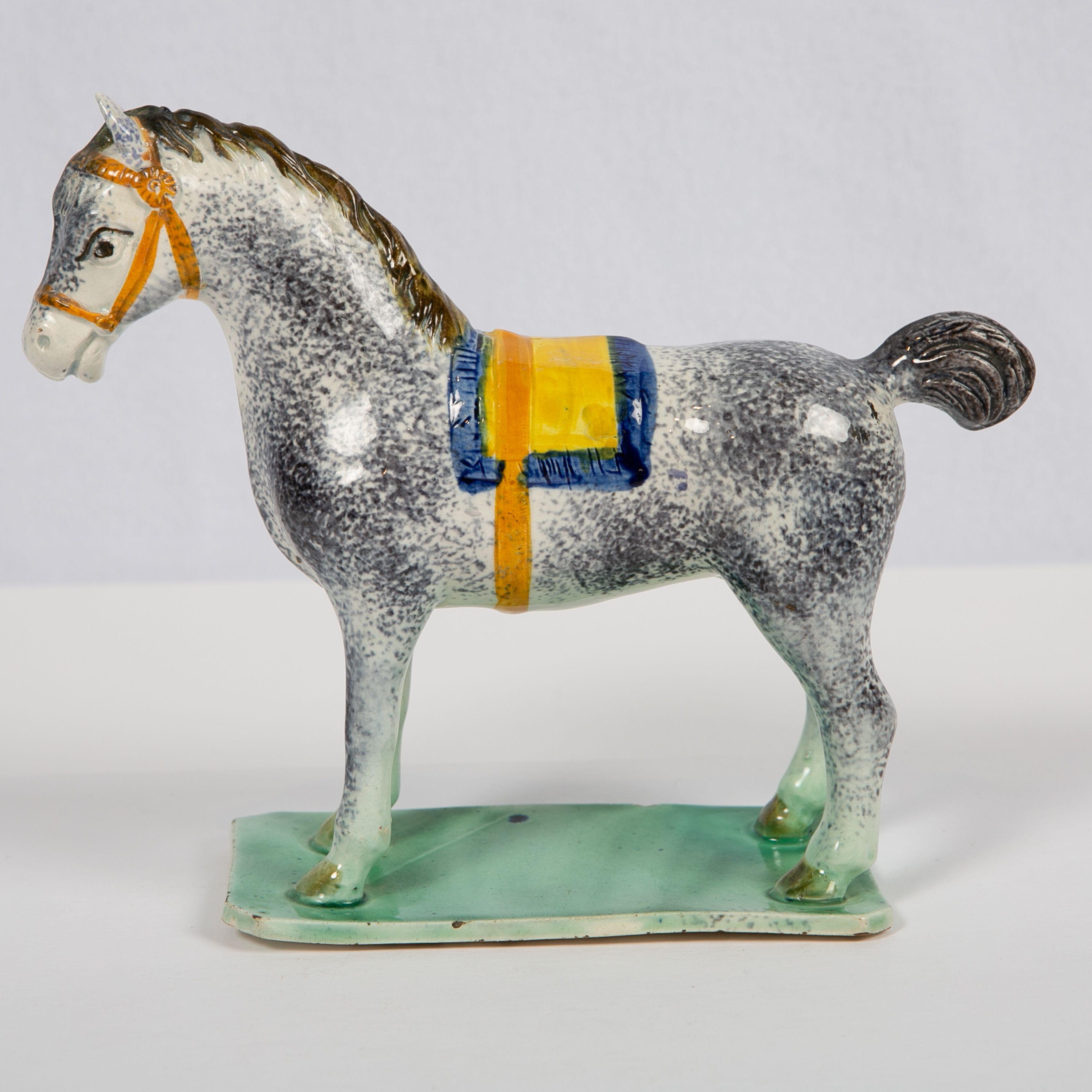 Provenance: with paper labels for the Zimmerman Collection and Art Trading Ltd.
This exceptional pearlware pottery figure of a saddled horse is charmingly rendered. The hand painted blue and yellow saddlecloth and orange halter highlight the