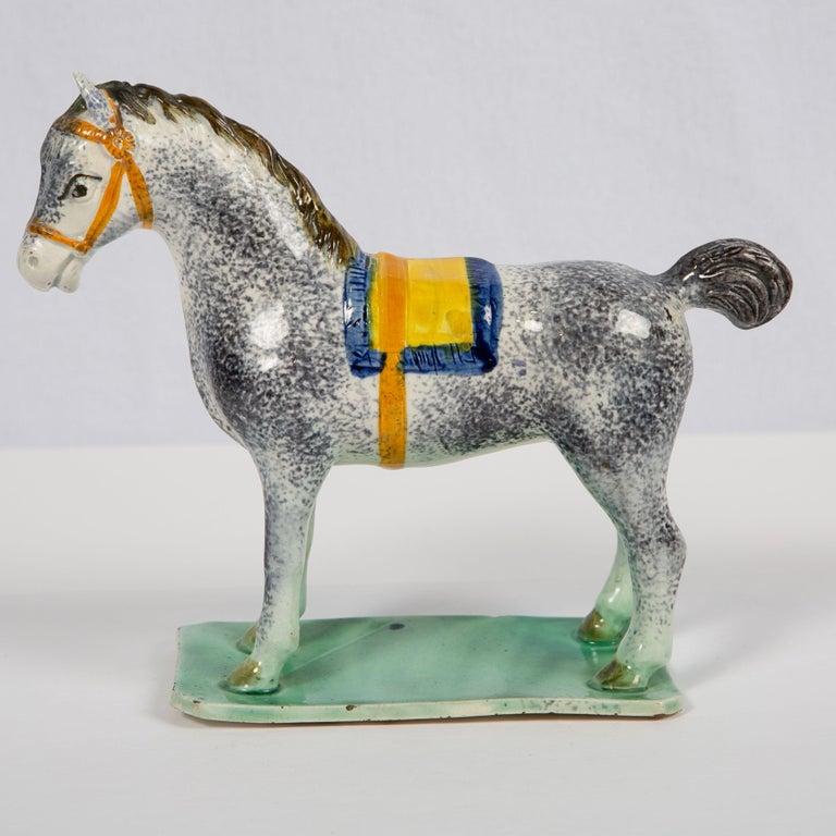 Provenance: with paper labels for the Zimmerman Collection and Art Trading Ltd.
This exceptional pearlware pottery figure of a saddled horse is charmingly rendered. 
The hand-painted blue and yellow saddlecloth and orange halter highlight the