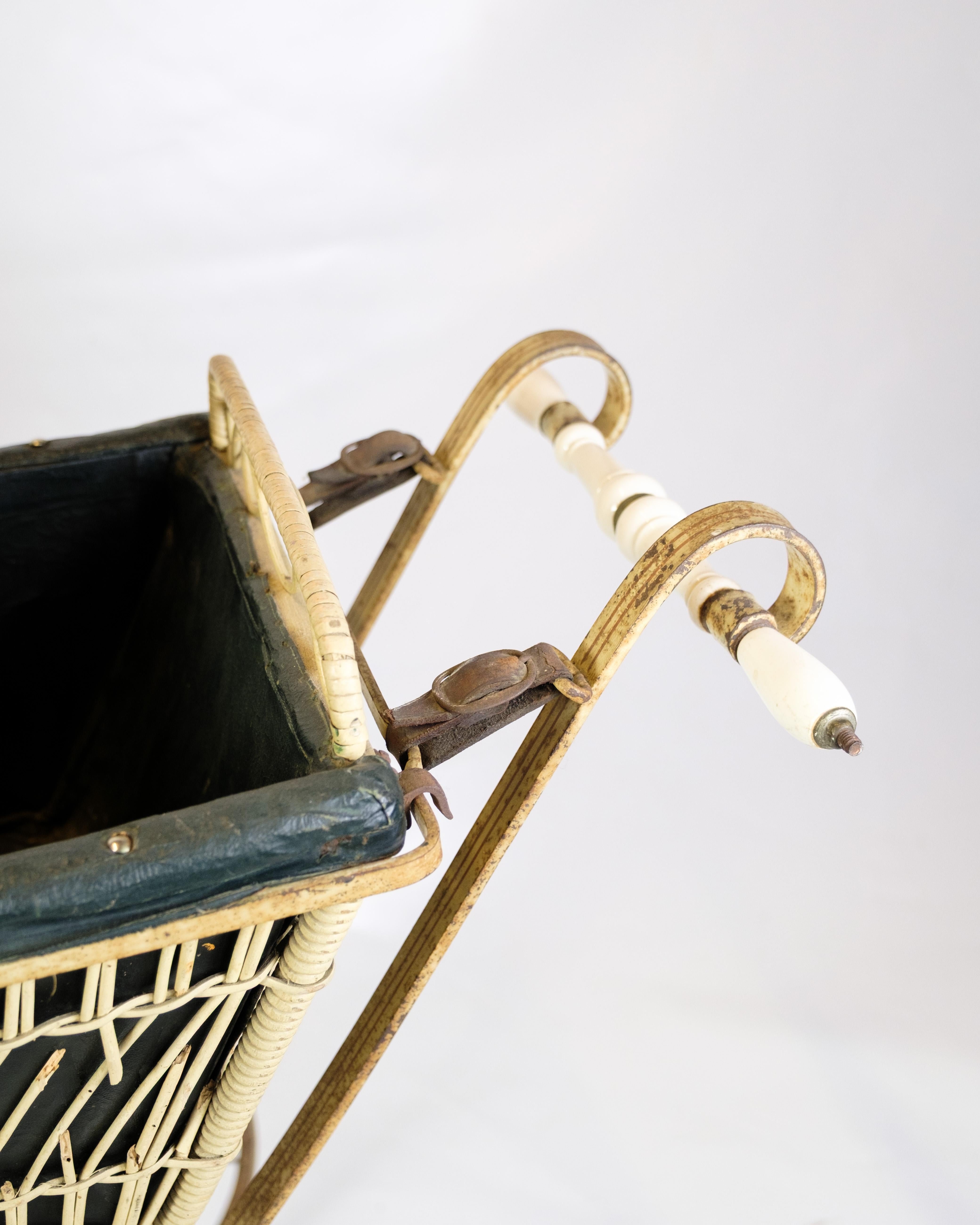 Carrozzina antica del 1900 circa con cesto in vimini e capottina originale. La carrozzina poggia su un telaio in metallo splendidamente curvato, con grandi ruote a raggi e maniglie bianche. Carrozzina classica e decorativa, ideale come oggetto da